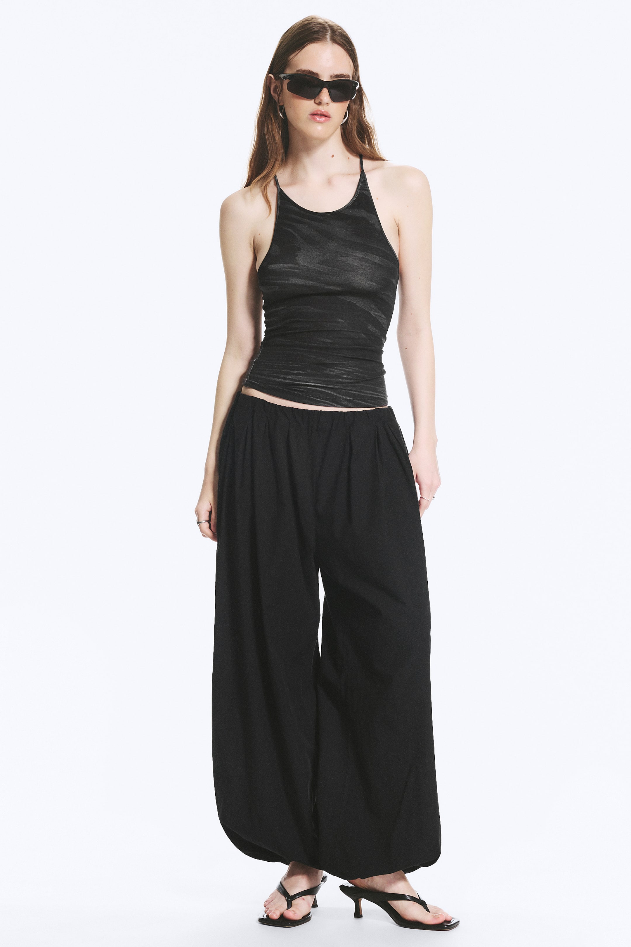 Ver imagen más grande: Pantalones negros de pierna ancha con cintura elástica y tobillos fruncidos, creando una silueta voluminosa tipo globo. La tela ligera y texturizada cae de manera suelta, con los pantalones presentados de frente.