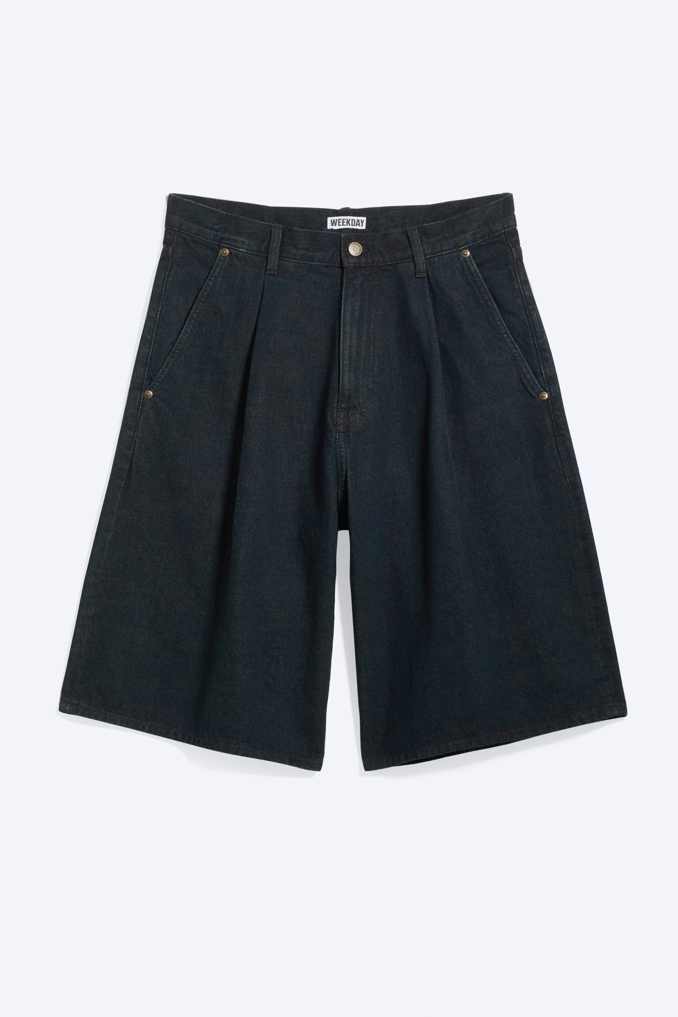 Zobrazit větší obrázek: Volné plisované šortky v tmavém praném pevném denimu mají přední zip s knoflíkovým zapínáním a šikmé boční kapsy. Viditelné přední záhyby definují široký střih nohavic, které končí nad kolenem.