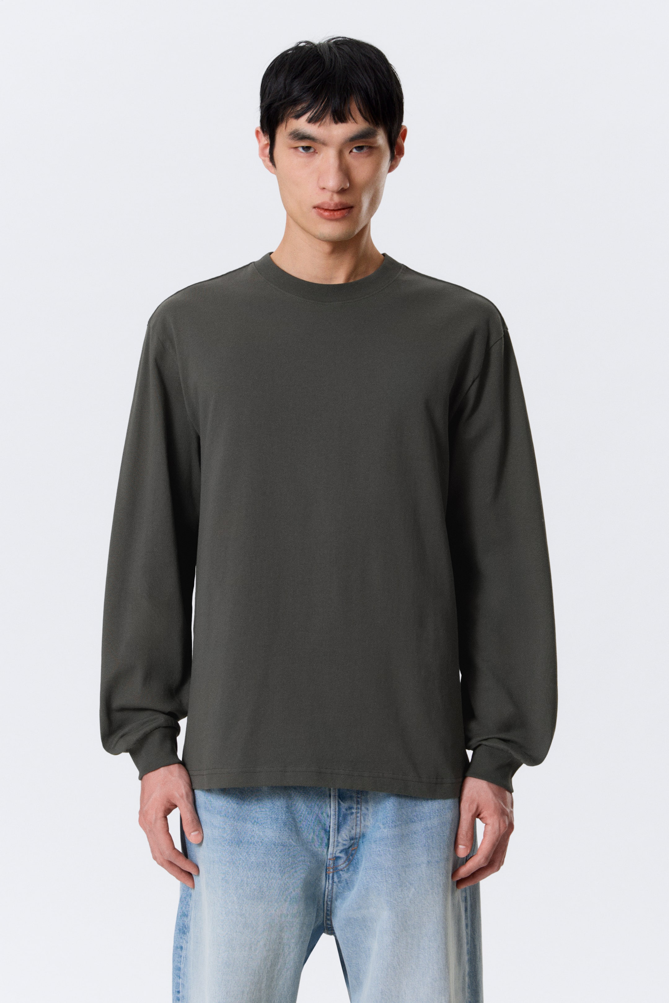 Vezi imaginea mai mare: Un tricou cu mânecă lungă de culoare gri închis este prezentat din față. Are un guler rotund, manșete cu nervuri și o croială lejeră.