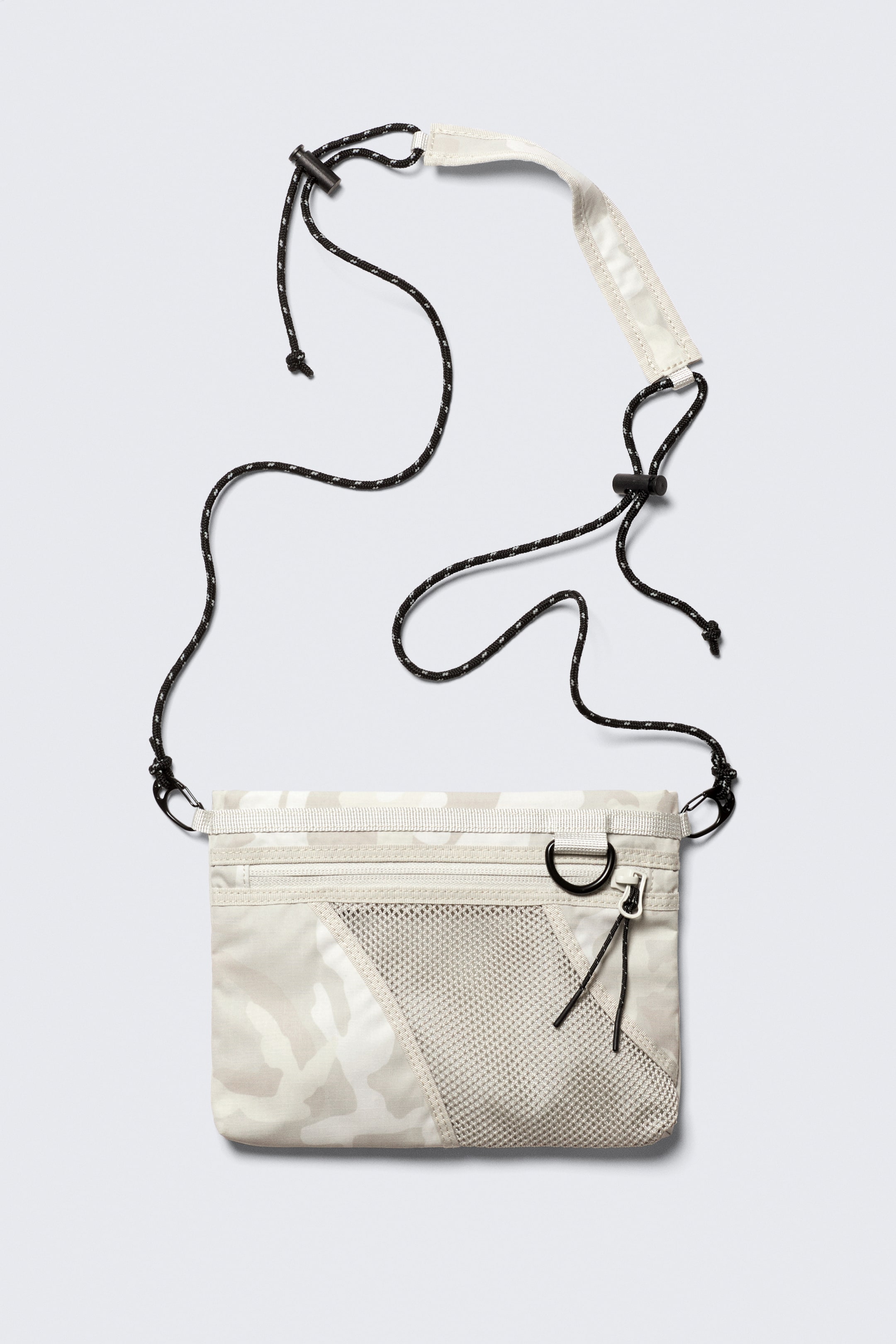 Grotere afbeelding bekijken: Het product is een mini crossbody tas, gepresenteerd VOOR, met een licht camouflagepatroon en een getextureerde afwerking op zijn rechthoekige lichaam. Het bevat een diagonale mesh-paneel en een buitenzak met rits aan de voorkant, en is uitgerust met een verstelbare koordschouderband met zwarte stoppers, clipbevestigingen en een bredere platte sectie.