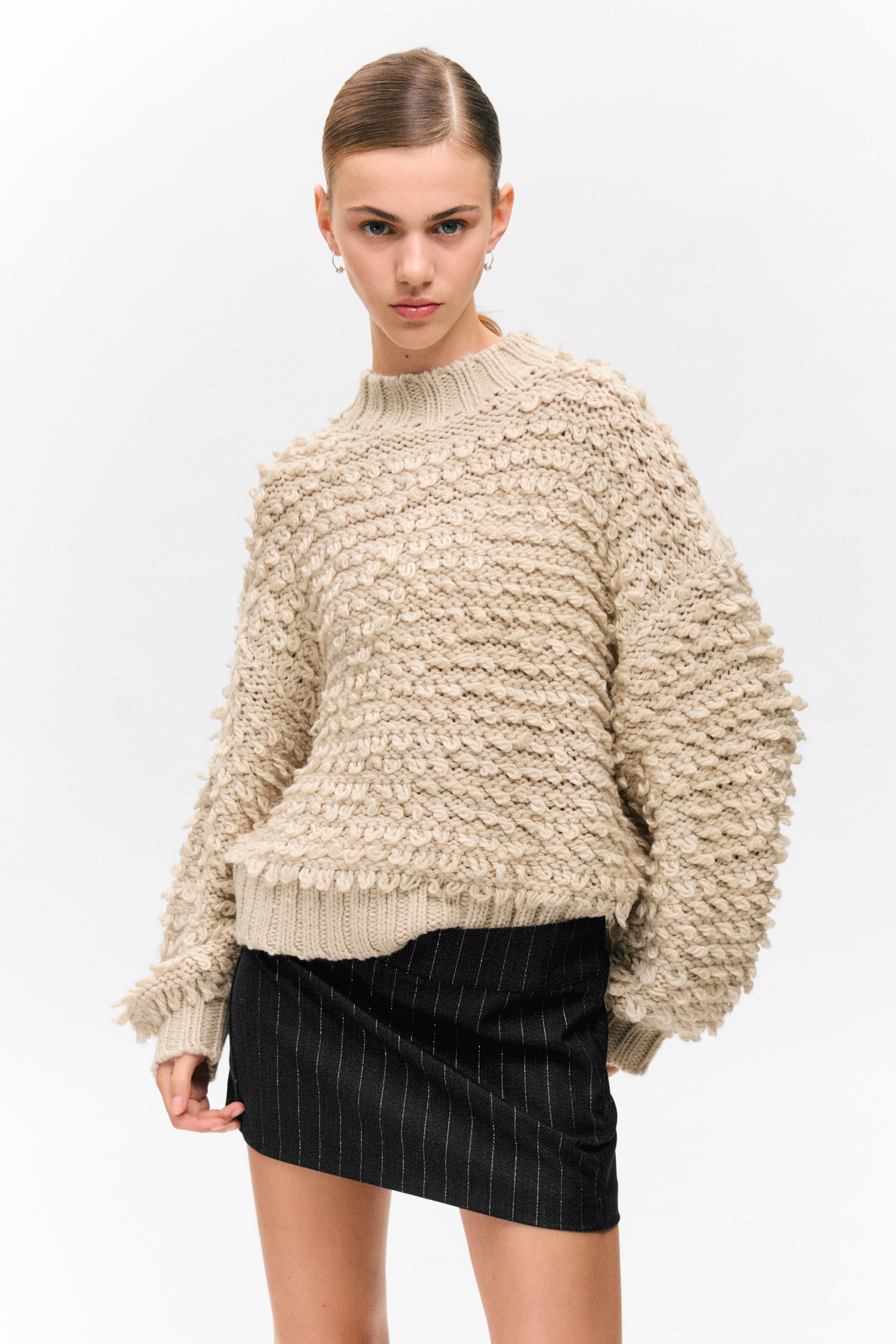 View larger image: A natural-toned sweater is being presented from the front, showcasing its chunky, textured knit with prominent loops. It is featuring a ribbed mock neck, ribbed cuffs, and a ribbed hem, all contributing to its relaxed, oversized fit.