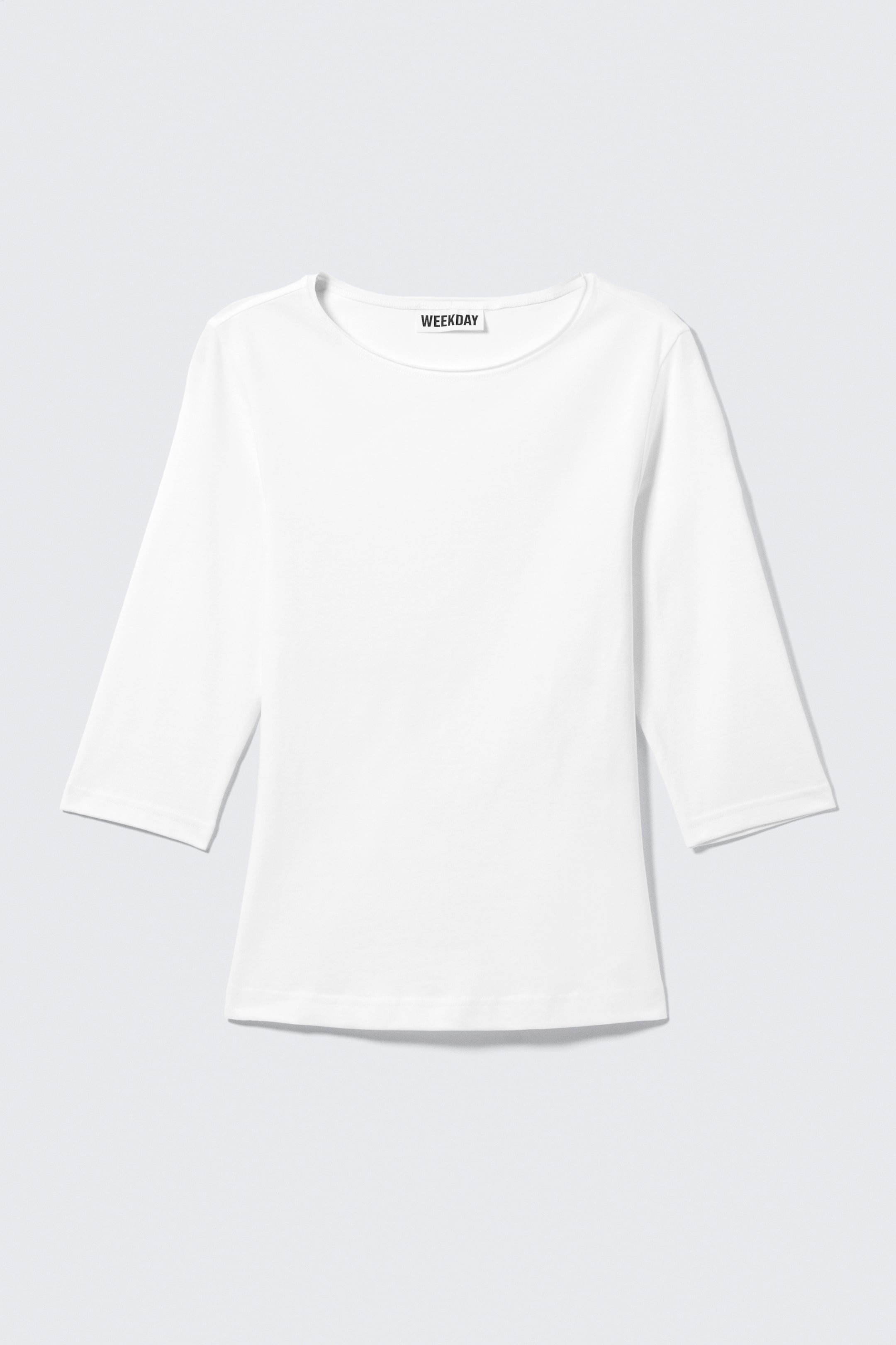 Näytä suurempi kuva: Valkoinen tyköistuva paita on esillä edestäpäin, ja siinä on pyöreä pääntie sekä kolme neljäsosaa pitkät hihat. Siinä on suorat helmat ja 'WEEKDAY'-merkkilappu näkyvissä pääntien takana.