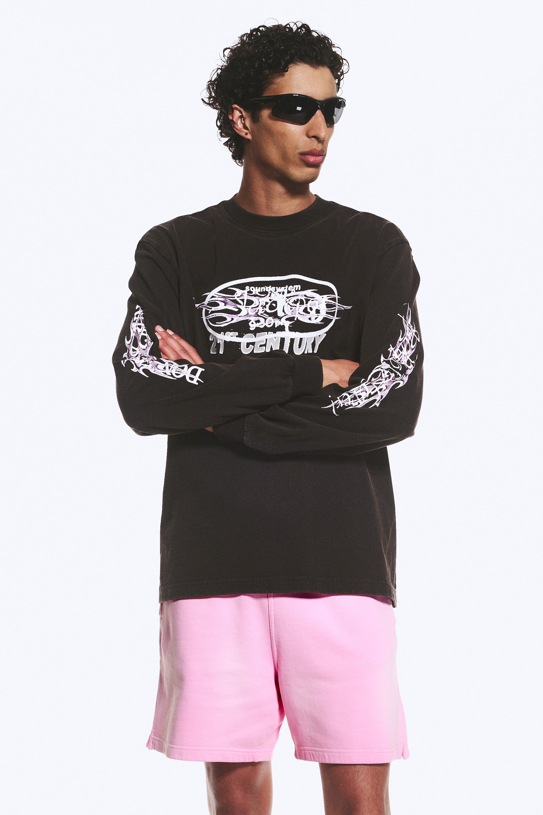 Visa större bild: En svart långärmad t-shirt med rund hals och avslappnad passform har en stor vit och lila oval grafik på framsidan, med stiliserad text inklusive "soundsystem" och "21st CENTURY." Matchande stiliserade vita och lila grafiker löper även längs båda ärmarna.