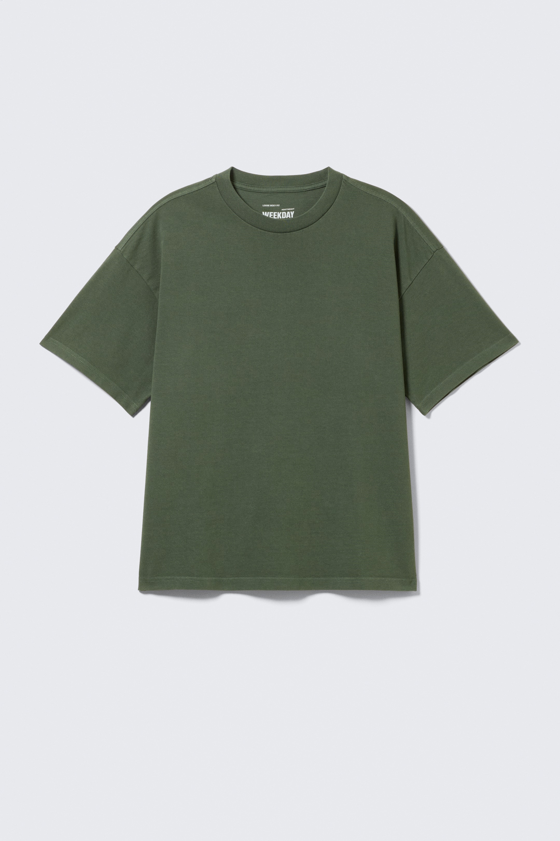 Visualizza immagine più grande: Una t-shirt oversize verde oliva è mostrata dal DAVANTI. È realizzata in jersey di cotone, con girocollo, spalle scese e maniche ampie, con un'etichetta bianca "WEEKDAY" visibile sul retro interno del collo.