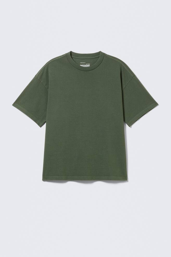 An olive green oversized T-shirt is being displayed from the front. It is crafted from cotton jersey, featuring a crew neck, dropped shoulders, and wide sleeves, with a white "WEEKDAY" label visible on the inner back neckline. - 1