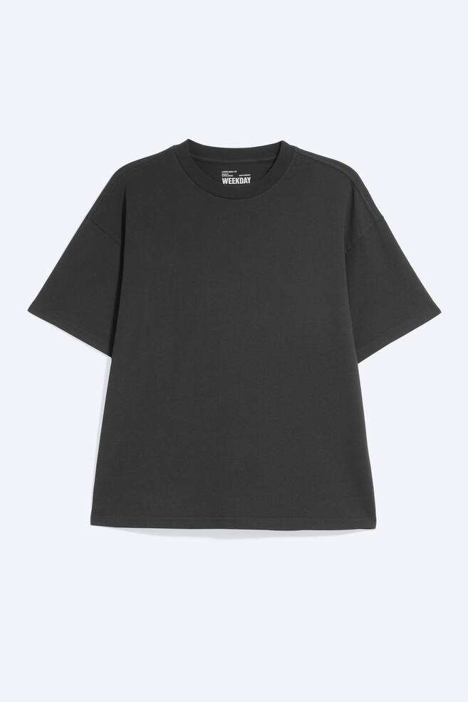 En mÃ¶rkgrÃ¥ T-shirt visas framifrÃ¥n, med en boxig, oversized passform med nedsÃ¤nkta axlar och vida korta Ã¤rmar. Plagget har en ribbad rund halsringning och en rak fÃ¥ll. - 1