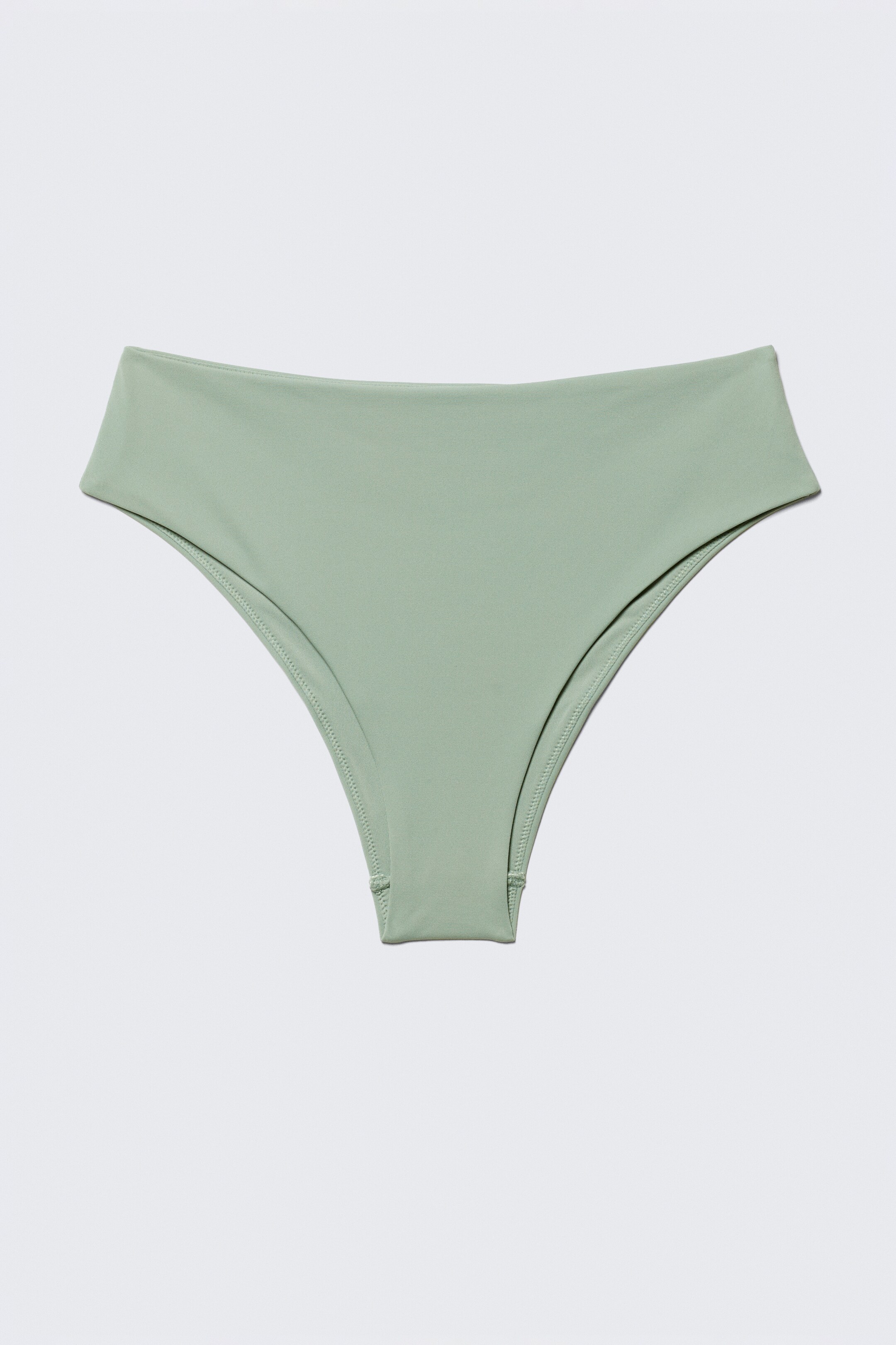 Visualizza immagine più grande: Un bikini a vita alta di colore verde pallido è disteso piatto, rivolto in avanti. Presenta aperture per le gambe alte e una fascia in vita liscia e piatta, con cuciture visibili che delineano le aree delle gambe e del tassello.