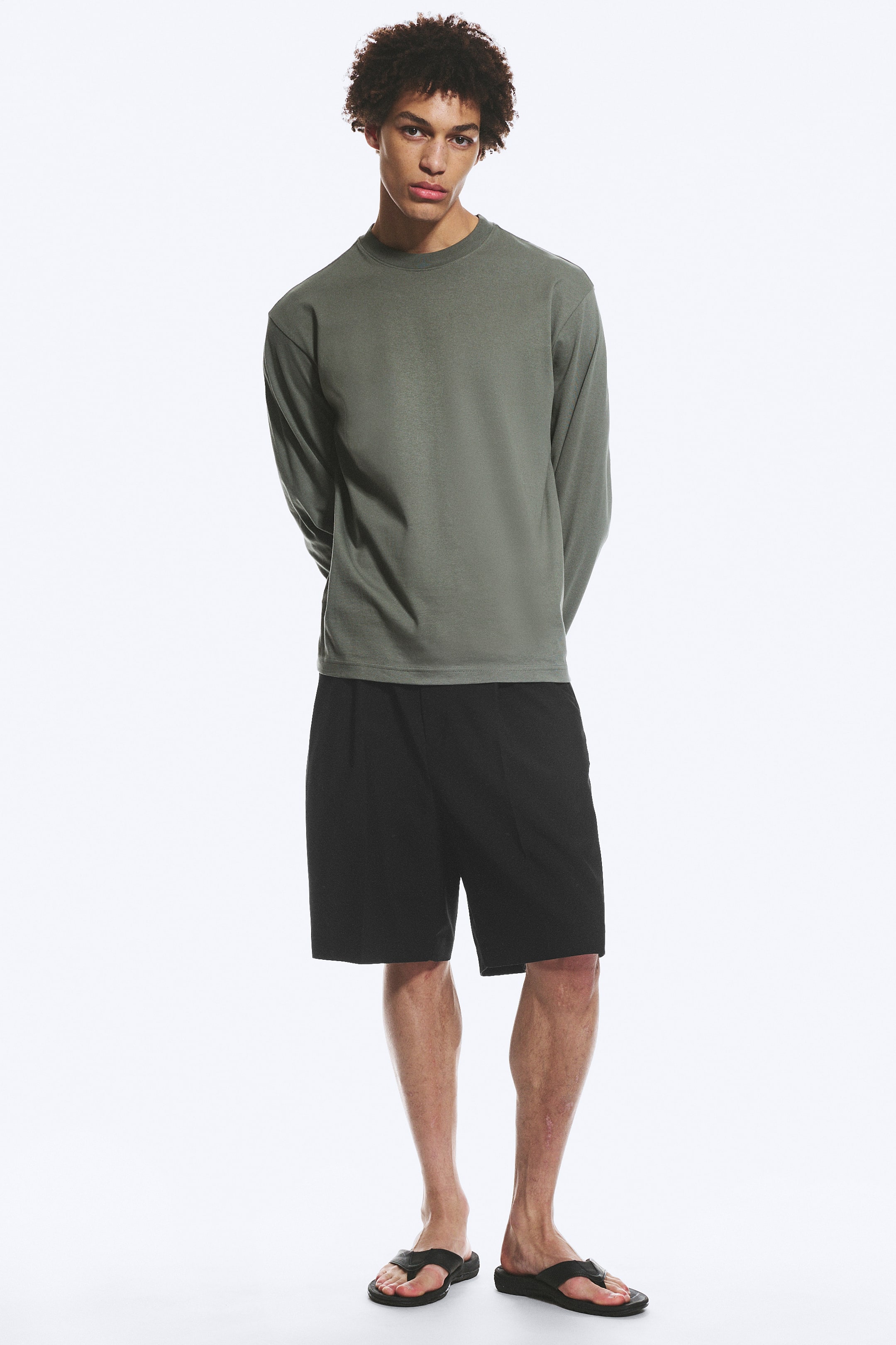 Ver imagen más grande: Se presenta una camiseta de manga larga en color verde oliva, vista de frente. Cuenta con un cuello redondo, un corte holgado y un dobladillo recto con puños sencillos, todo en un tejido liso y mate.
