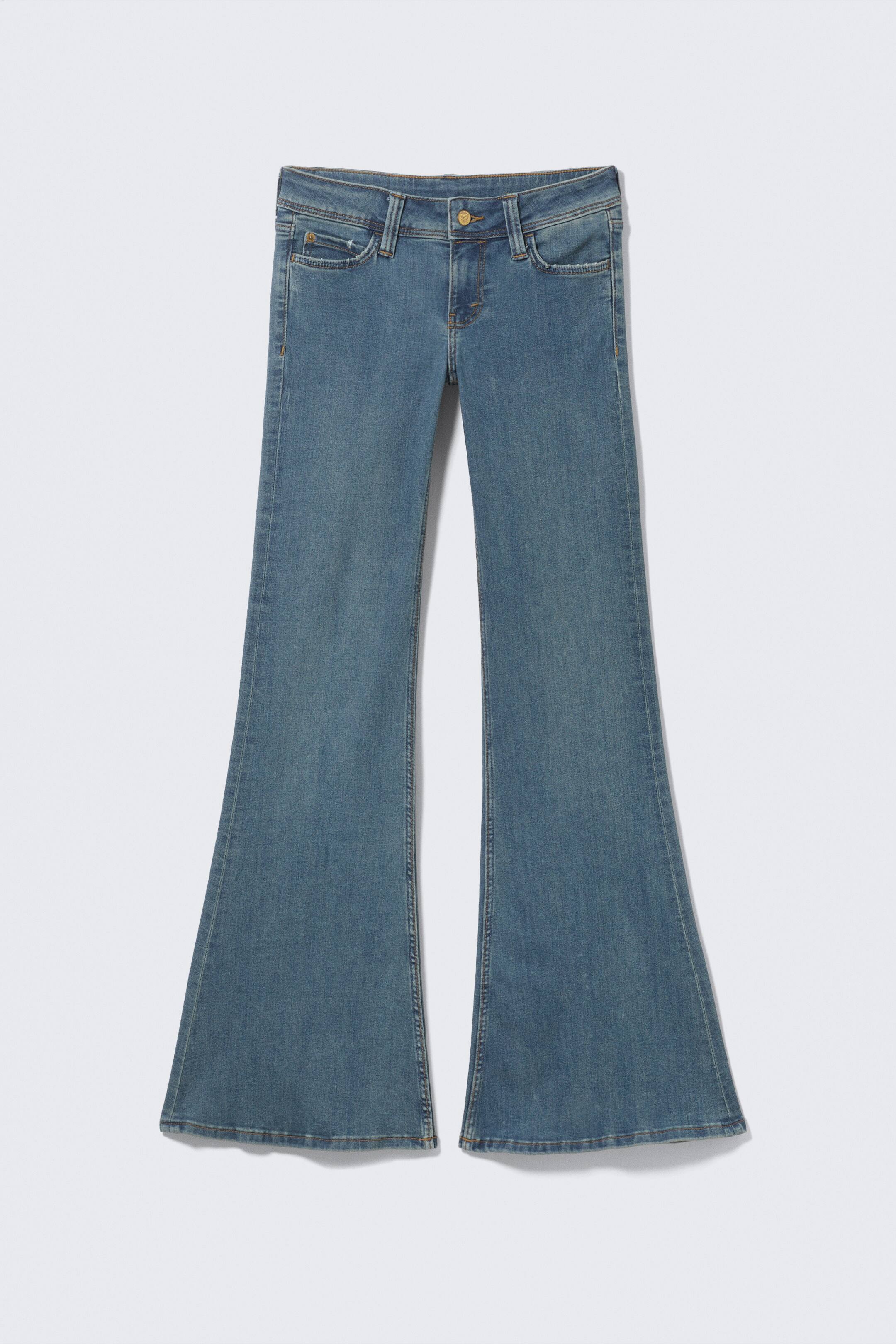 Visualizza immagine più grande: Un paio di jeans in denim blu medio presenta il suo FRONTE, con una vita bassa, una vestibilità aderente sulla coscia e un'ampia svasatura dal ginocchio fino a una lunghezza lunga. I jeans mostrano una zip visibile, una chiusura con un solo bottone, passanti per la cintura e due tasche frontali con un taschino per le monete.
