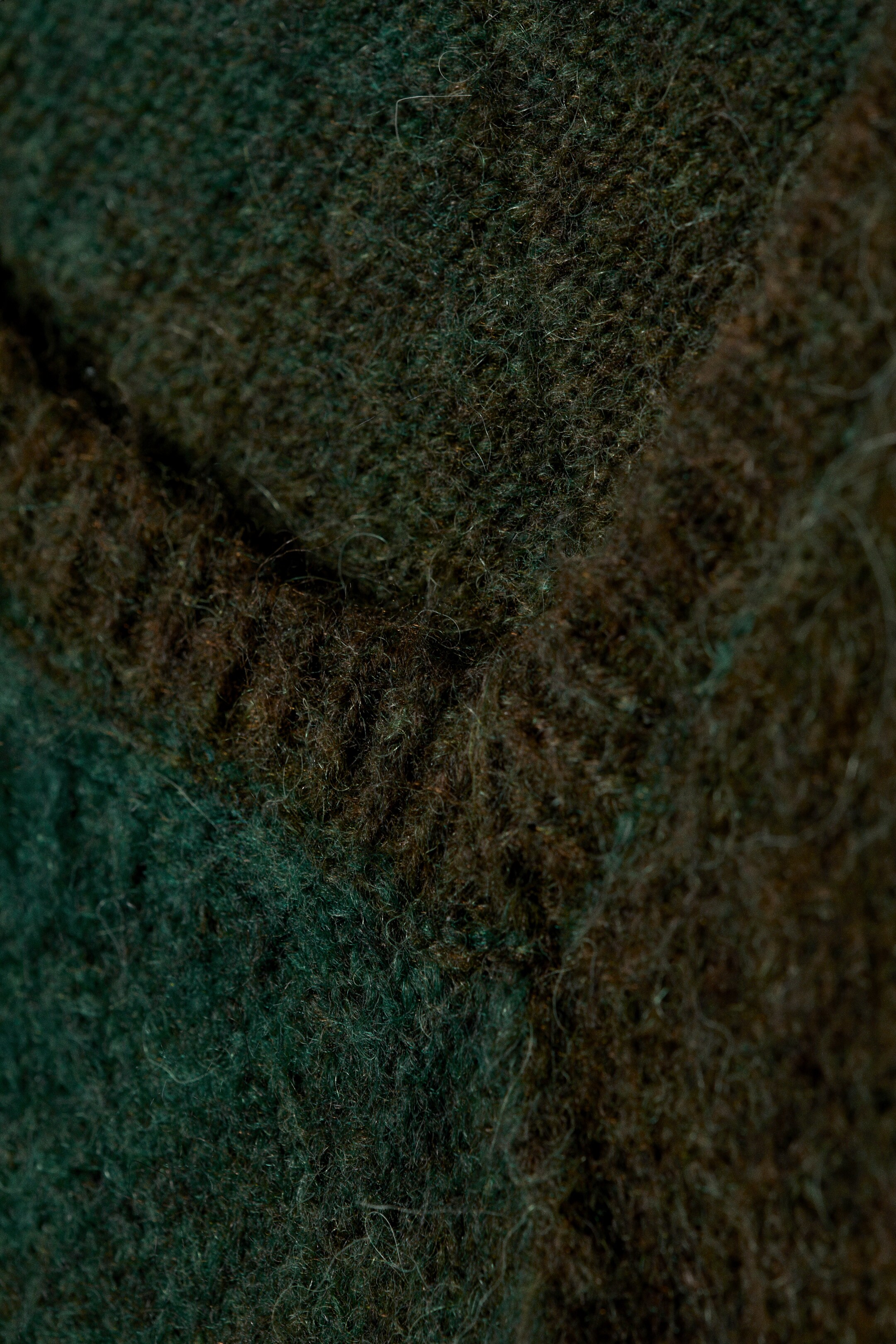 Vis større bilde: Et mykt tekstil viser et nærbilde av sin fibrøse tekstur, med et rutemønster i dype grønne og brune toner. En diagonal fold går over stoffet.