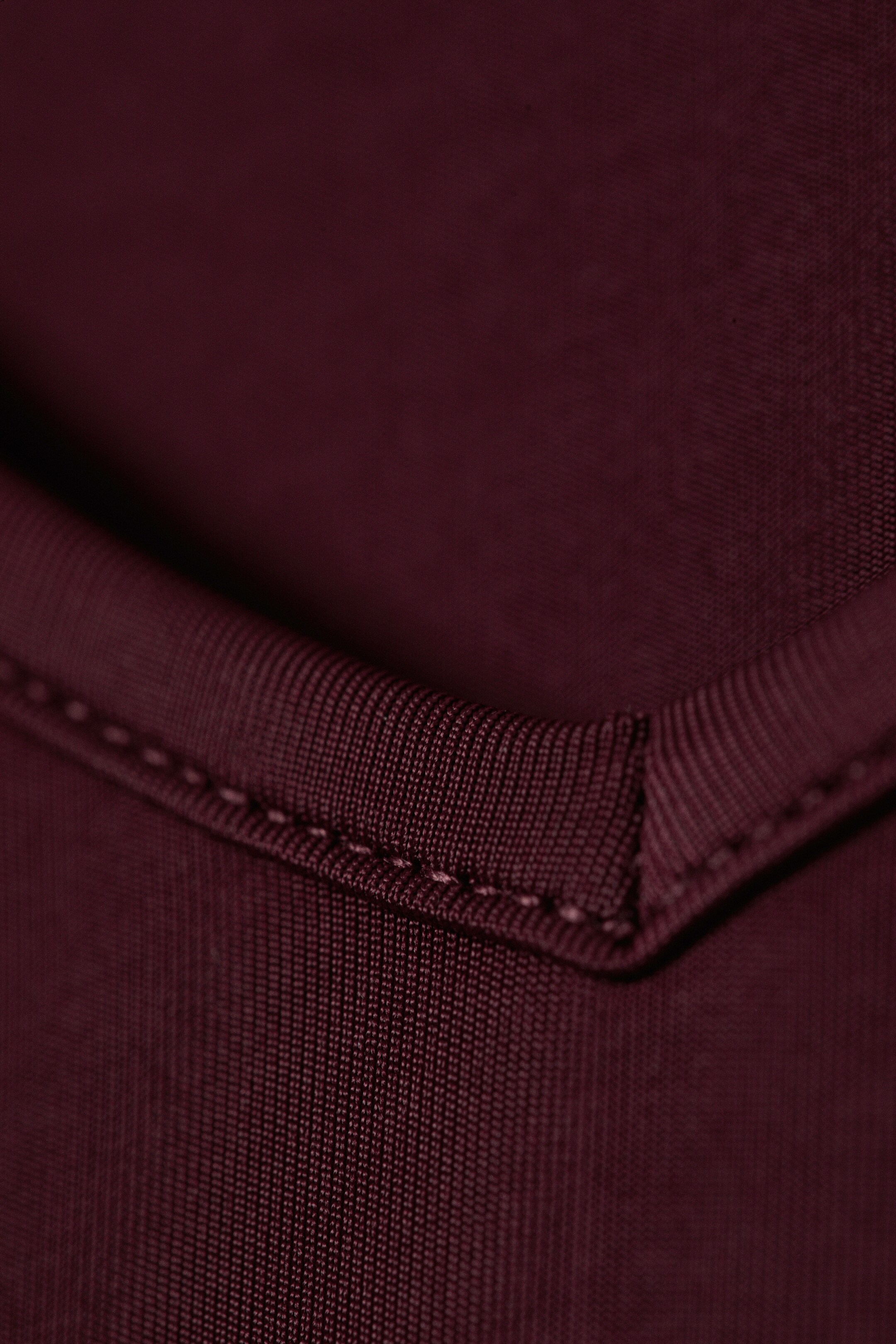 Agrandir l'image: Un vêtement bordeaux présente un gros plan d'une couture piquée. Le tissu affiche un tissage subtil, avec une finition plus prononcée et finement texturée le long du bord plié, où un fil assorti forme un coin net et précis.