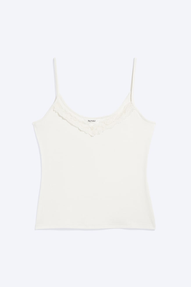 Un camisón blanco roto se muestra desde el frente, con finos tirantes tipo espagueti y un escote en V. Un delicado encaje adorna el escote, y el nombre de la marca 'MONKI' es visible en una etiqueta debajo del encaje. - 1