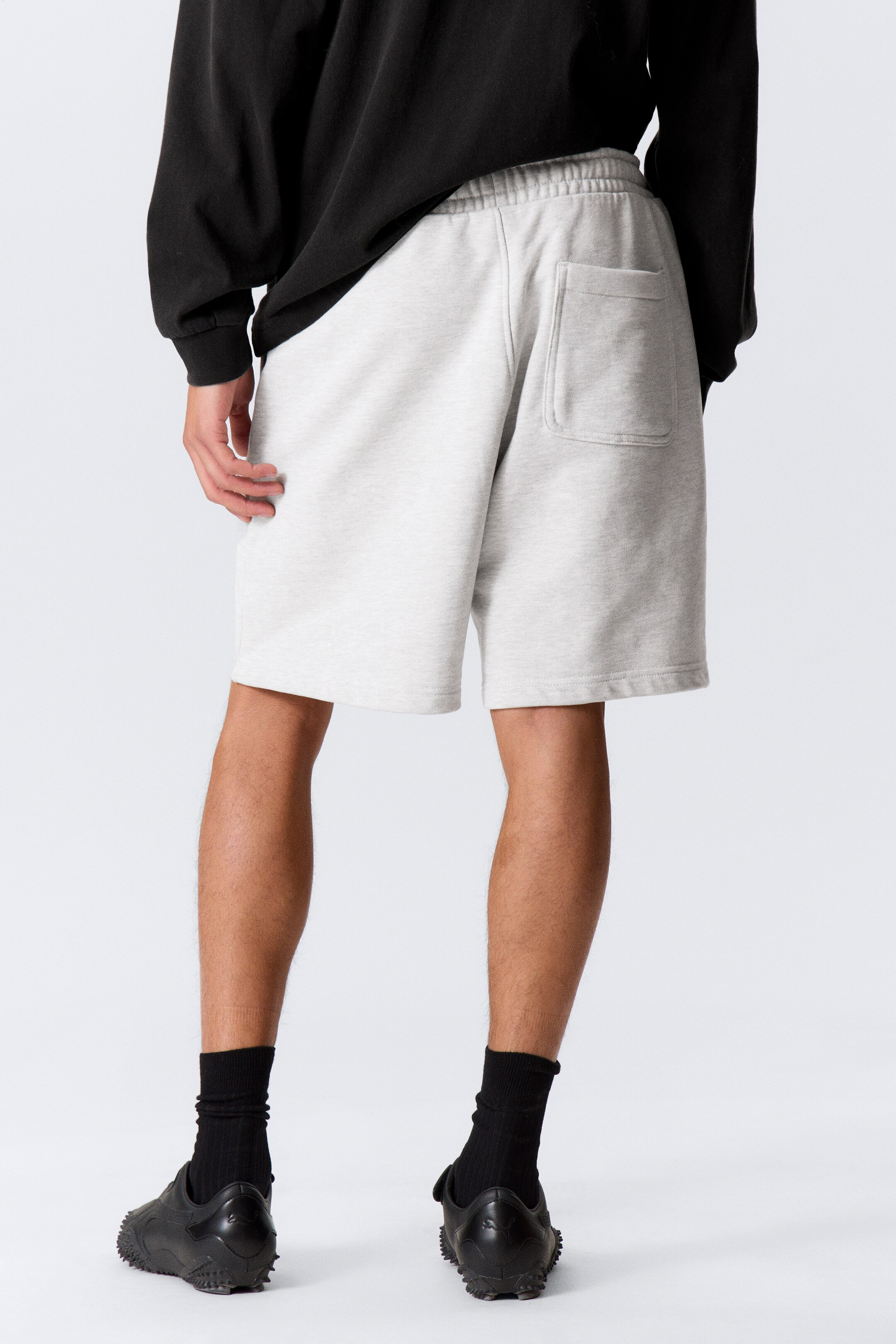 Grotere afbeelding bekijken: Heather grijze sweat shorts worden van achteren getoond, met een elastische tailleband en een enkele opgestikte zak aan de rechterkant achter. De shorts zijn in een ontspannen pasvorm gesneden, eindigend boven de knie met een rechte zoom.
