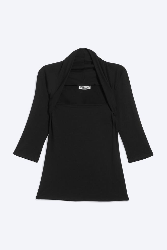 Un haut en maille noir est prÃ©sentÃ© Ã  plat, de face, avec un design superposÃ© comprenant une couche de base Ã  encolure droite sous un empiÃ¨cement type shrug intÃ©grÃ©. LâempiÃ¨cement prÃ©sente des manches trois-quarts et un col drapÃ© enveloppant le cou et les Ã©paules. - 1