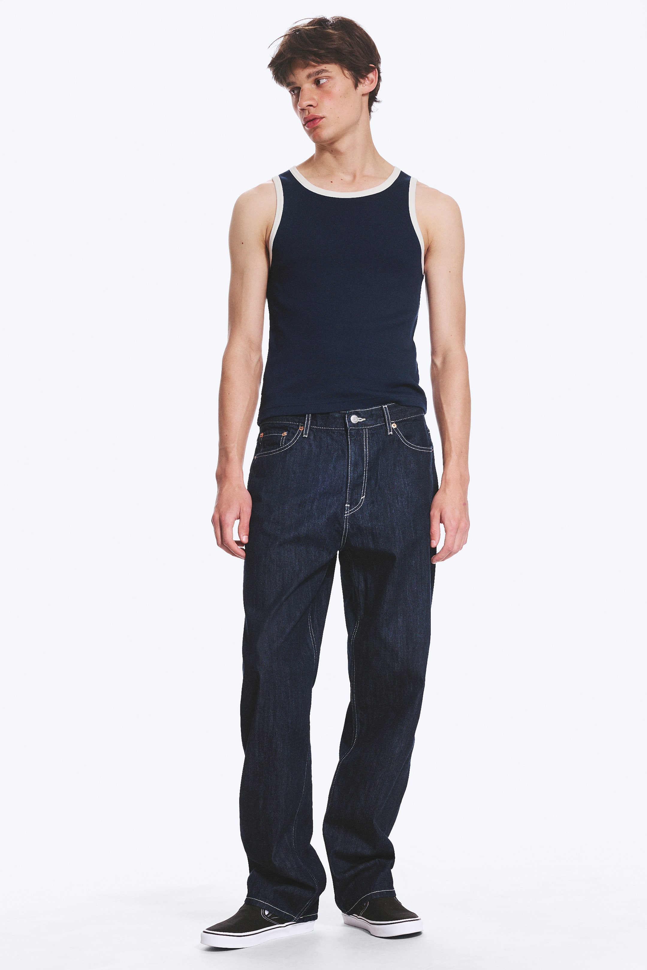 Visualizza l'immagine ingrandita: Jeans in denim lavaggio scuro vengono presentati, caratterizzati da una vestibilità rilassata a gamba larga, cuciture a contrasto bianche evidenti sulle cuciture, tasche e patta, e una chiusura con bottoni visibili e cerniera.