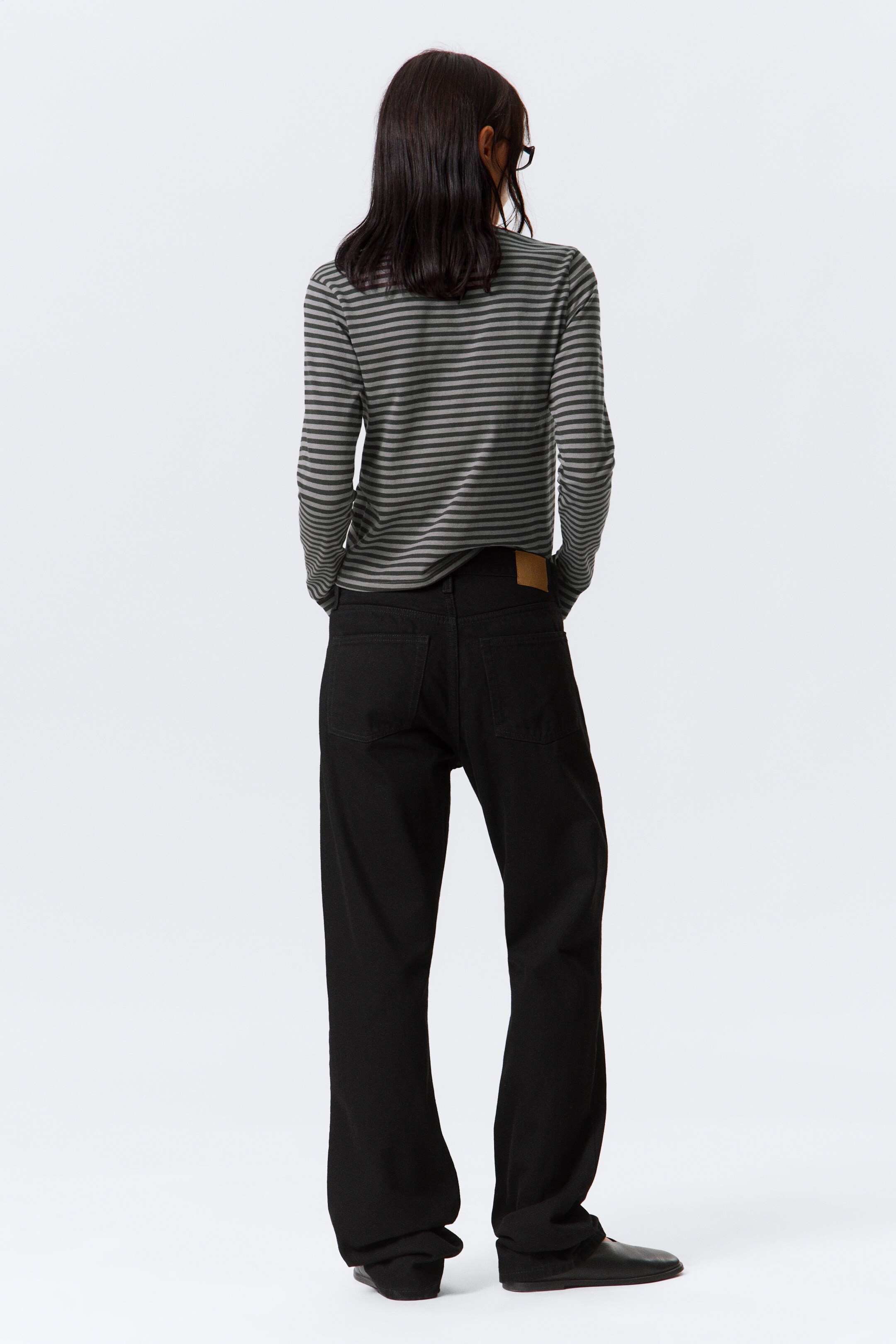 View larger image: A long-sleeved striped shirt in dark gray and olive green is being worn, seen from the back, fitting loosely. It is paired with black wide-leg pants, also seen from the back, featuring visible back pockets and a light brown patch on the waistband, with the legs pooling at the ankles over black flat shoes.