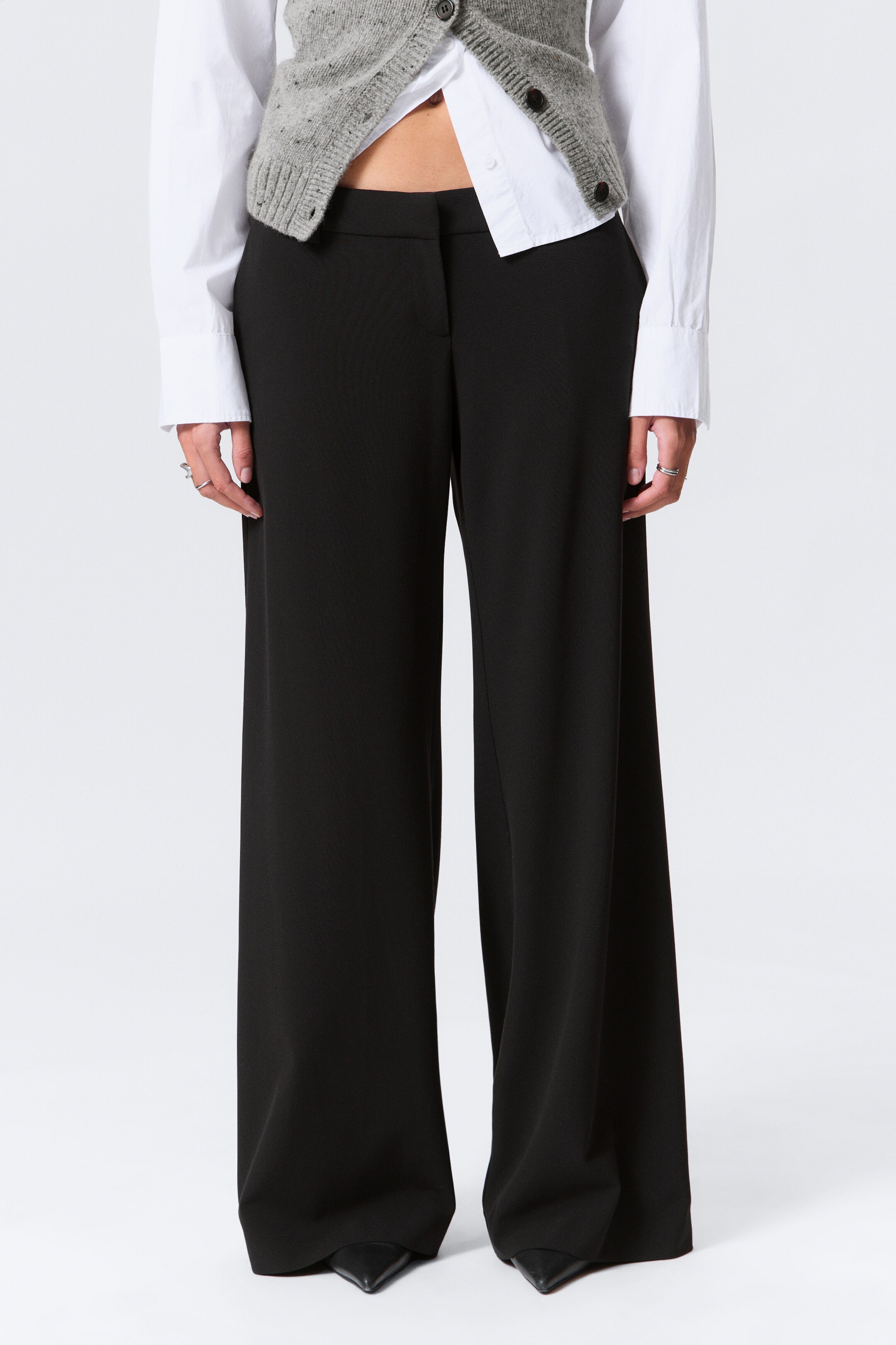 Visualizza immagine più grande: Pantaloni neri a gamba larga sono presentati frontalmente, con un design a vita alta e frontale piatto. I pantaloni cadono con un drappeggio fluido, estendendosi a una lunghezza intera che si accumula leggermente sopra le scarpe a punta.