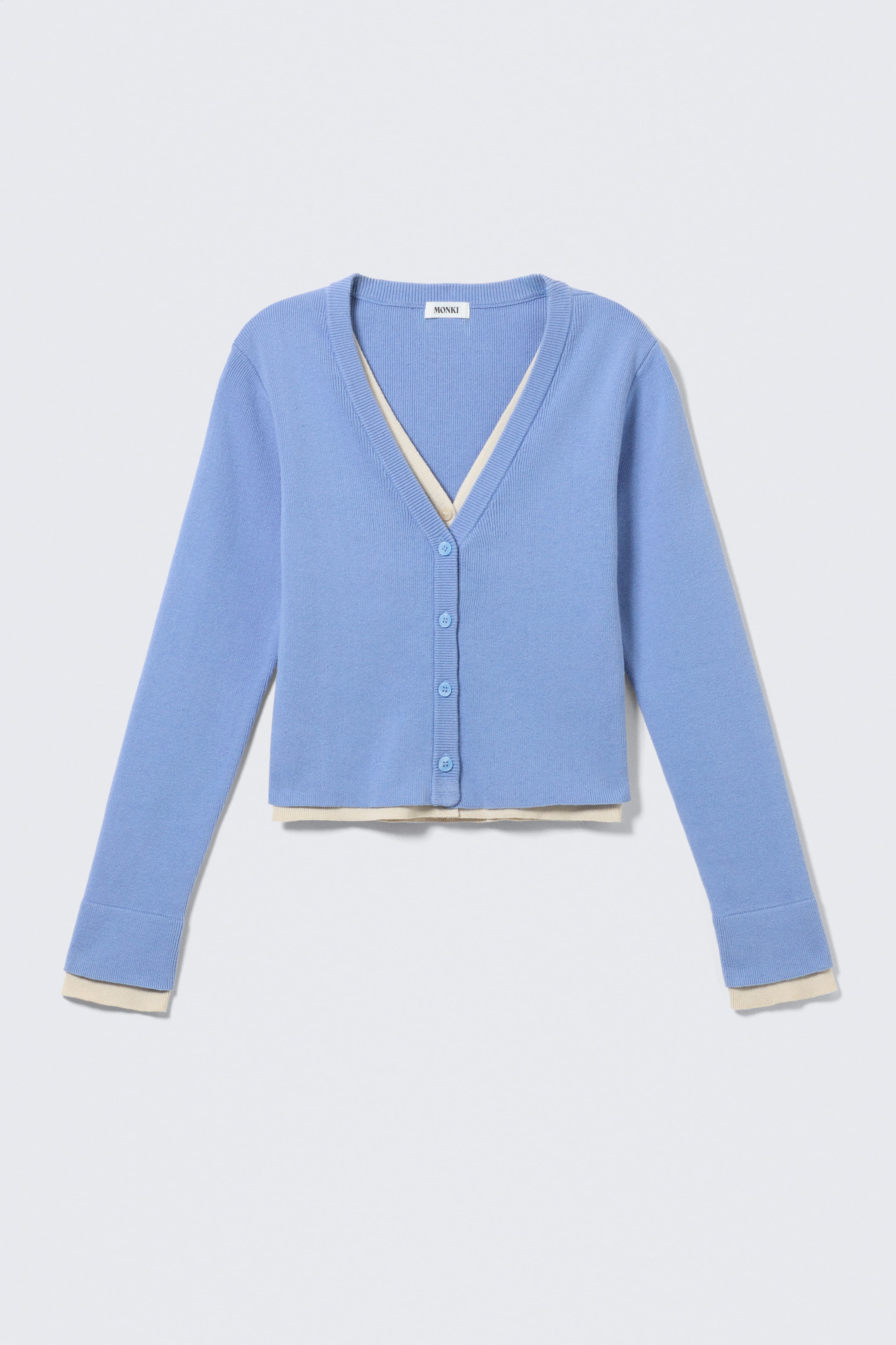 Agrandir l'image: Un cardigan bleu de la marque FRONT présente un col en V, six boutons assortis bleus le long de son centre, et des poignets et un ourlet côtelés. Une couche de couleur crème est visible en dessous, apparaissant au niveau du col en V, de l'ourlet du bas et des poignets des manches.