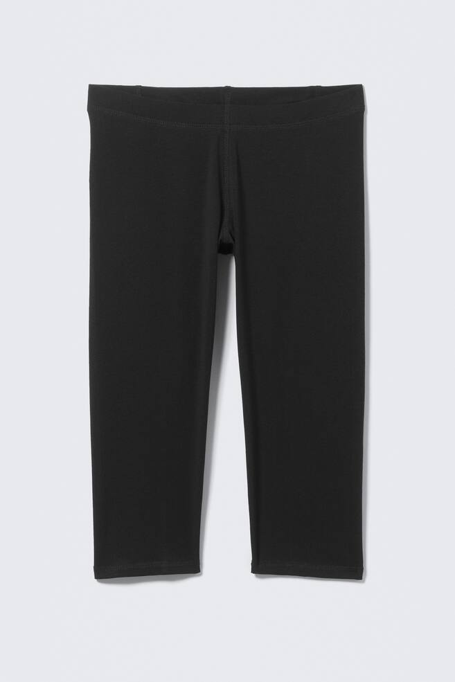 Sort capri-leggings præsenteres FORAN, med et glat, tætsiddende design, en bred, flad linning og en længde, der slutter lige under knæet. - 1