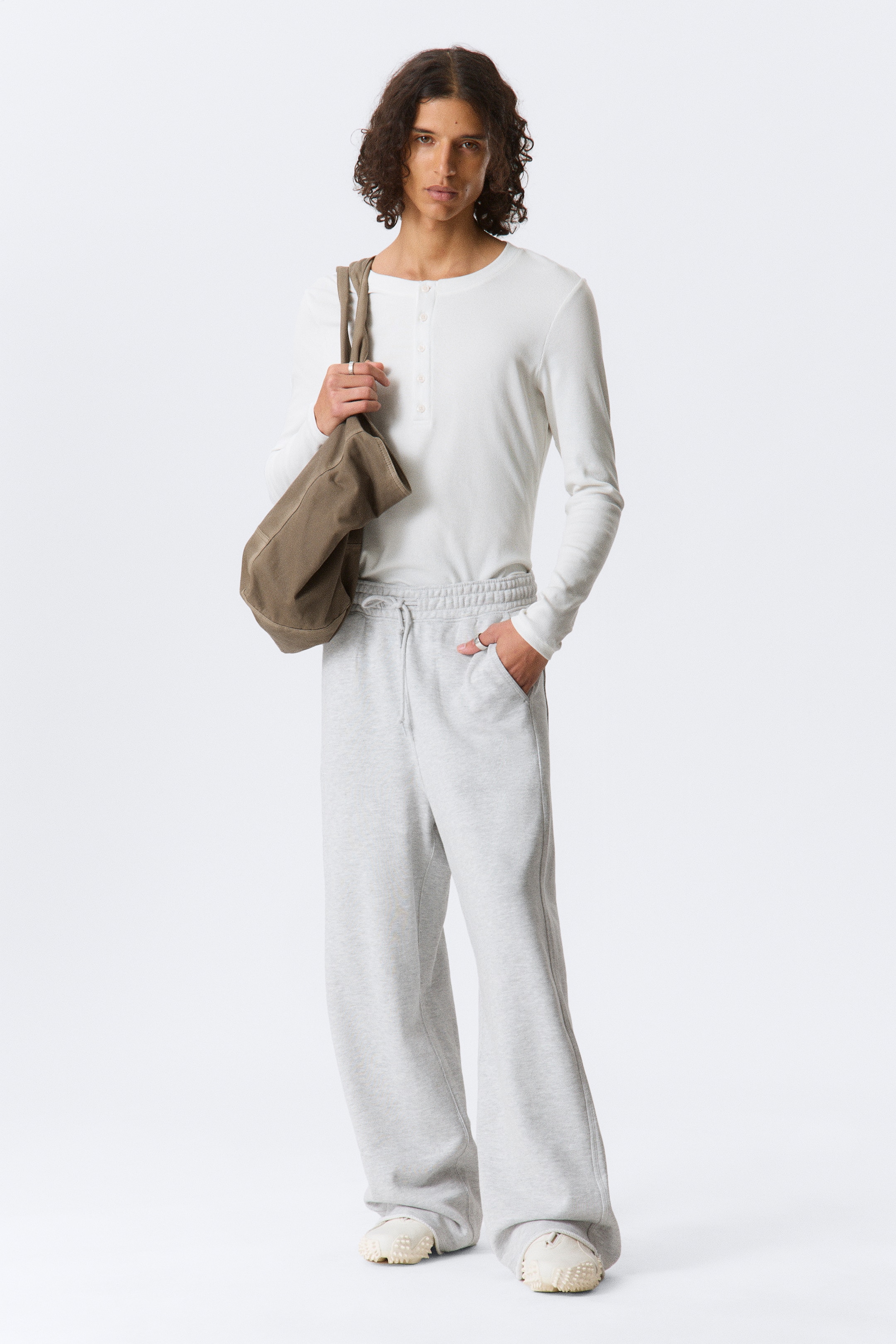 Grotere afbeelding bekijken: Een witte Henley-shirt met lange mouwen zit strak, met een geribbelde textuur en een vierknopen-sluiting. Lichtgrijze sweatpants met wijde pijpen bieden een losse pasvorm met een elastische tailleband met trekkoord en zijzakken.