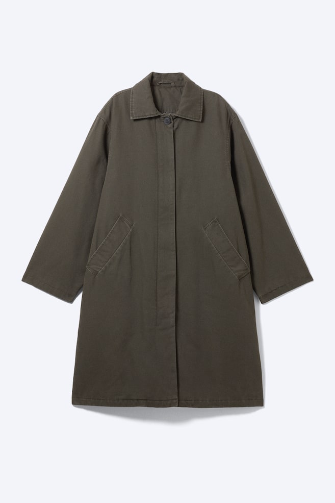 A loose-fitting, dark olive green car coat is shown from the front, featuring a point collar with a single visible top button and a concealed front placket. The coat is designed with angled welt pockets and long, wide sleeves, presenting a clean and utilitarian silhouette. - 1