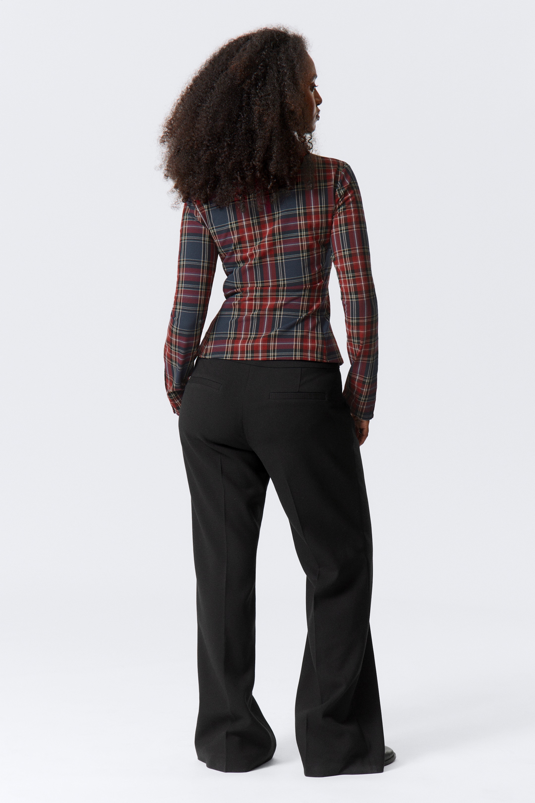 Größeres Bild anzeigen: Ein langärmeliges Oberteil und schwarze Hosen werden von hinten präsentiert. Das Oberteil ist mit einem rot, marineblau und gelb karierten Design gemustert und erscheint an der Taille tailliert. Die schwarzen Hosen zeigen eine entspannte, weit geschnittene Passform, die sich zum Saum hin ausstellt.