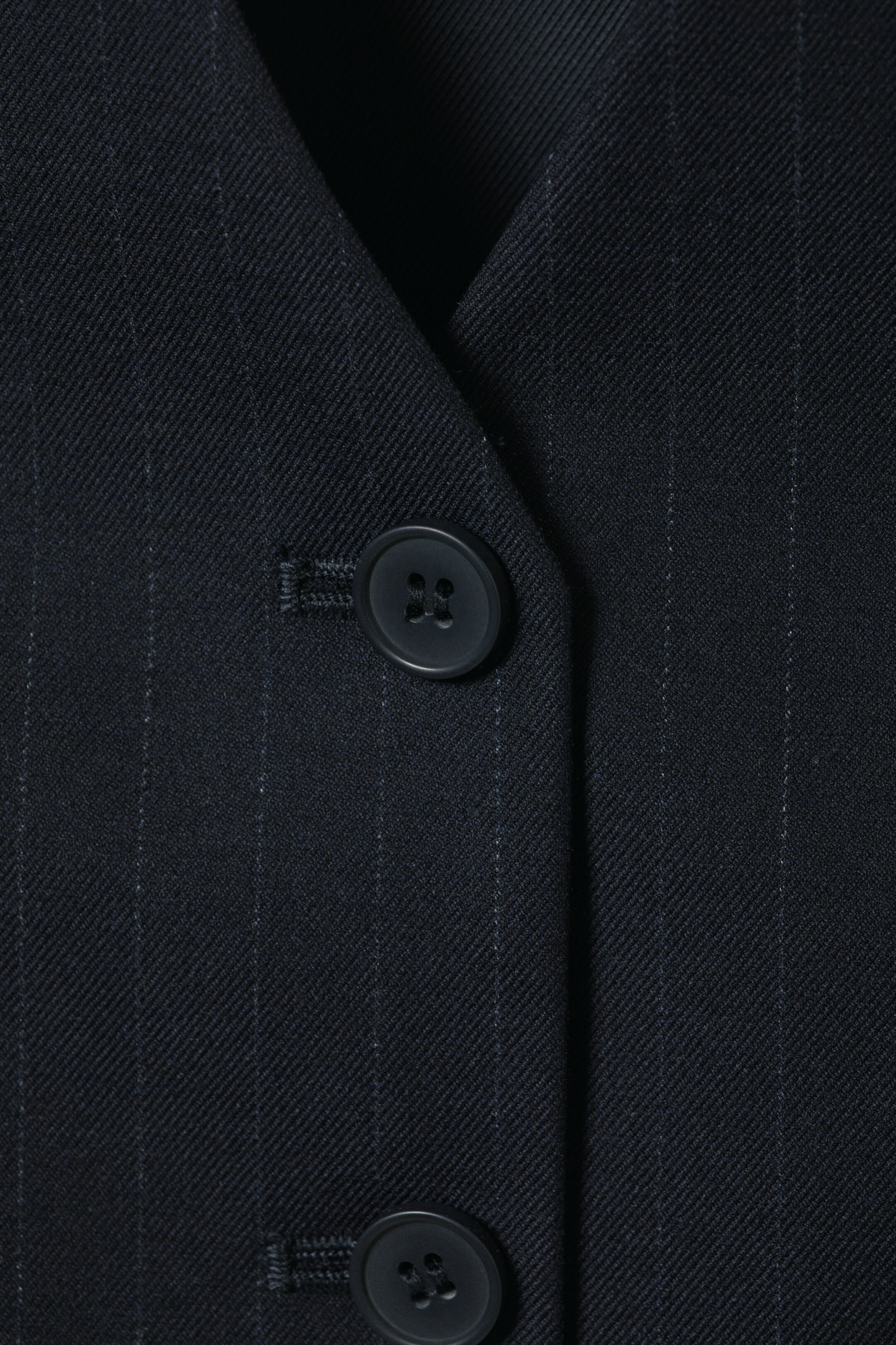 Agrandir l'image: Le gilet présente un gros plan de son tissu à fines rayures sombres, avec une fermeture à boutons à l'avant composée de deux boutons sombres à quatre trous et d'une boutonnière.