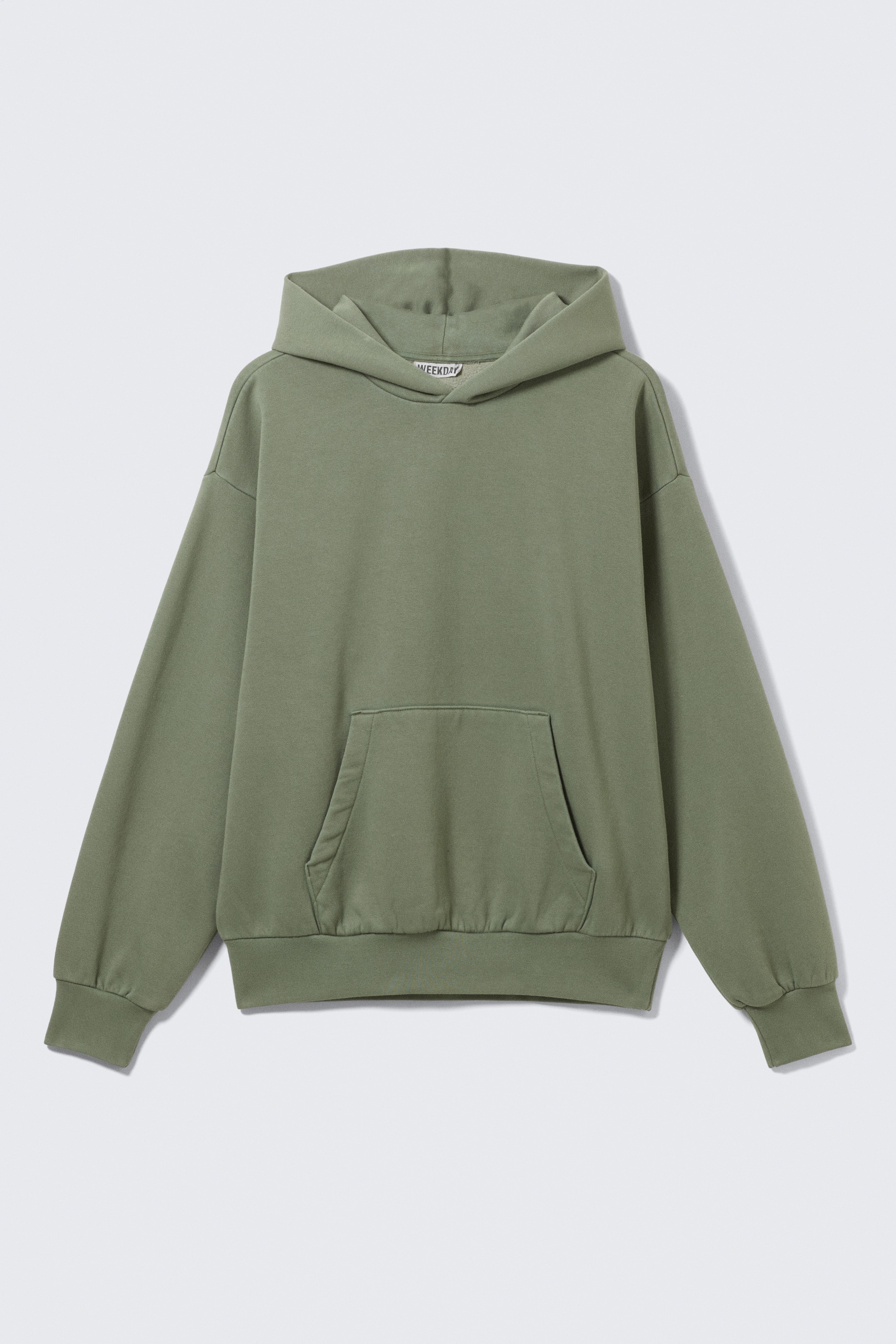 Agrandir l'image: Un sweat à capuche vert est présenté de FACE, avec une coupe ample et une structure douce aux épaules tombantes. Il présente une construction de capuche pliée, une poche kangourou spacieuse et des bordures côtelées avec un léger froncement aux poignets et à l'ourlet, créant une silhouette détendue et arrondie.