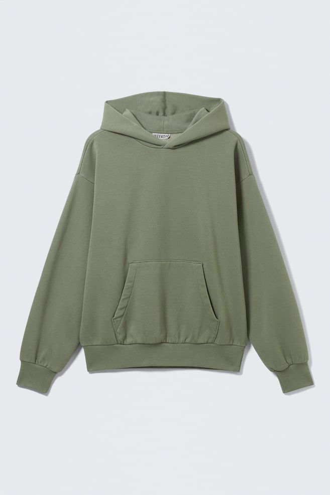 A green hoodie is presenting FRONT, featuring a loose fit and soft structure with dropped shoulders. It is showcasing a folded hood construction, a roomy kangaroo pocket, and ribbed trims with subtle gathering at the cuffs and hem, creating a relaxed, rounded silhouette. - 1