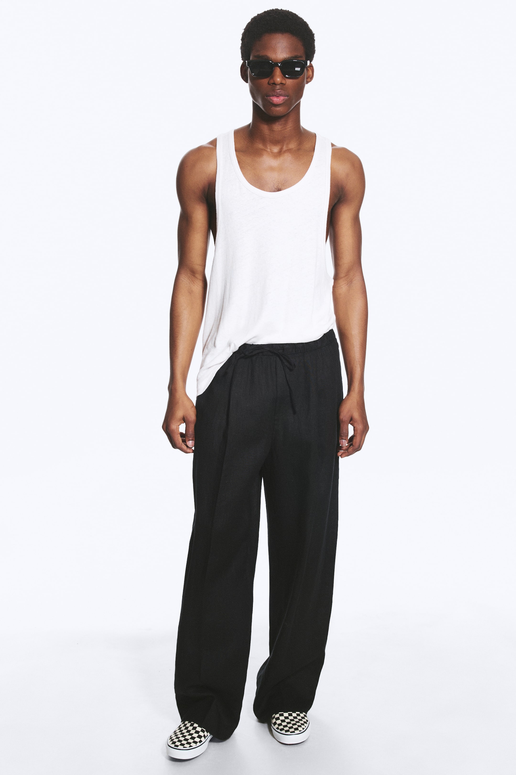 Agrandir l'image: Pantalon noir à jambes larges affichant une coupe décontractée et ample. Un cordon de serrage visible ajuste la taille, et leur tissu texturé tombe fluidement jusqu'aux chevilles.