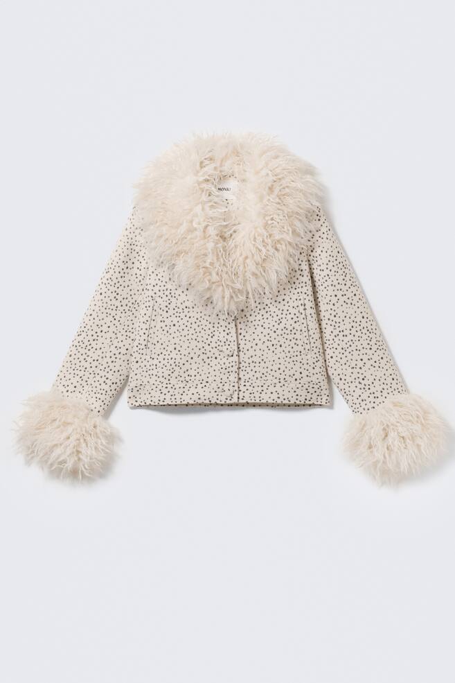 A cream-coloured jacket is presenting its front, featuring a speckled pattern of irregular dark dots across its body. It is designed with a large, shaggy cream faux fur collar and matching faux fur cuffs, and fastens with three visible buttons down the centre front. - 1