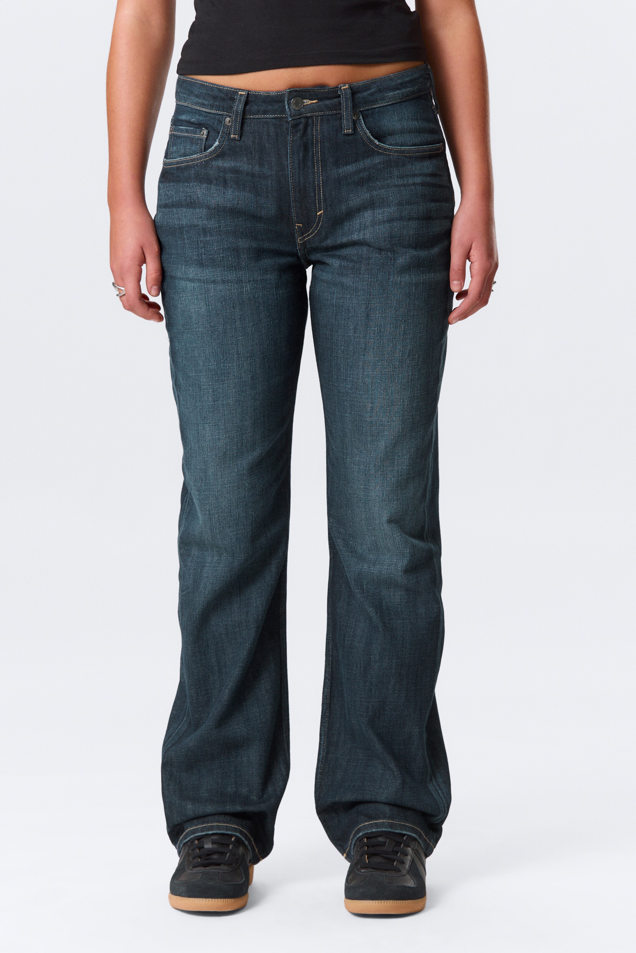 Ver imagen más grande: Los vaqueros de denim de lavado oscuro se presentan en una vista frontal, con una cintura de talle medio, un diseño de cinco bolsillos, cierre de botón y cremallera, y costuras en contraste. Se observa un ligero efecto desgastado y descolorido en los muslos, y el corte recto cae sobre unas zapatillas negras.