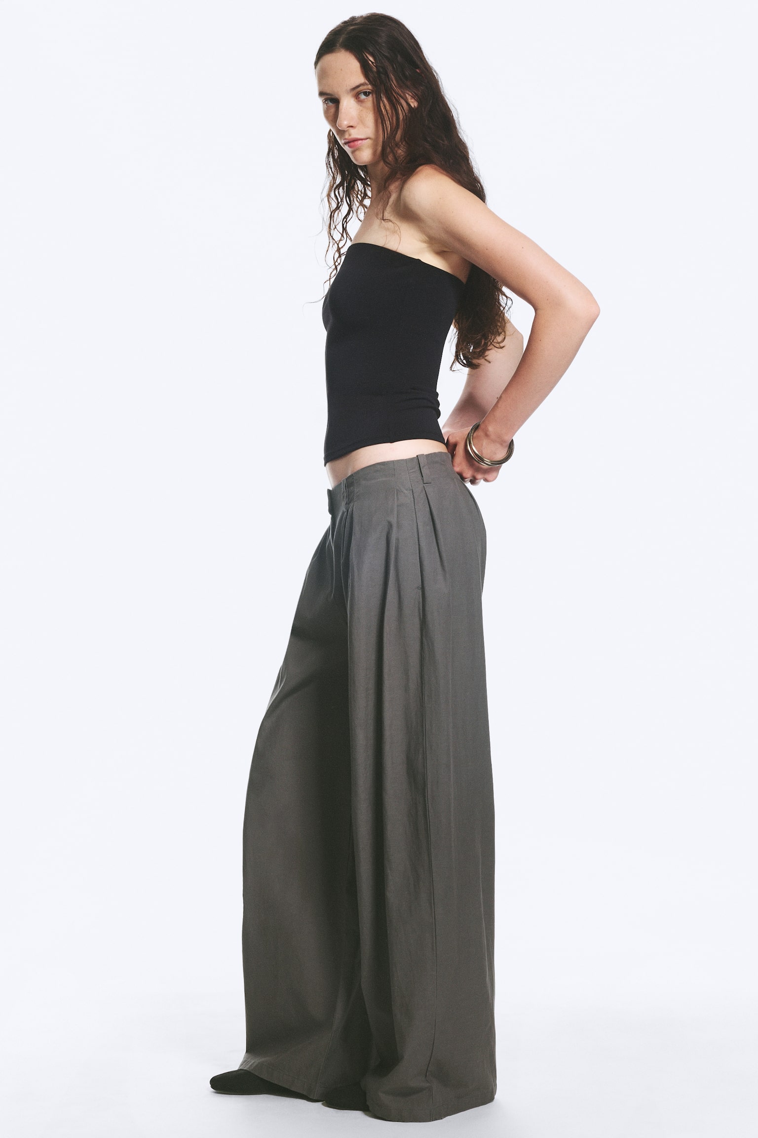 Un pantalon à plis est présenté de face, avec des jambes larges et des détails cousus. Le pantalon est doté de passants de ceinture, de poches latérales et d'une fermeture à crochet et zip au centre à l'avant. - 1