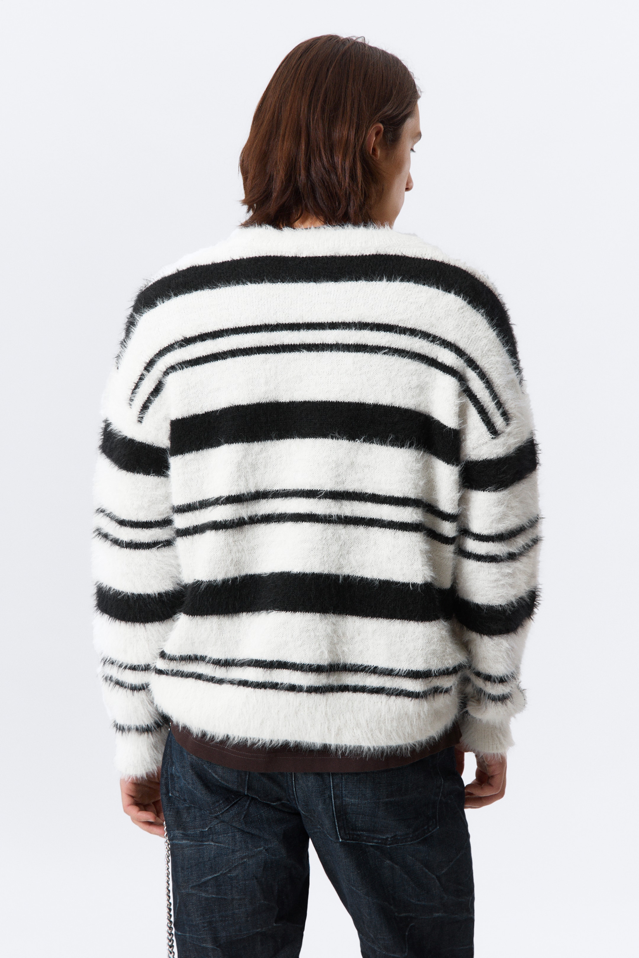 Größeres Bild anzeigen: Ein schwarz-weiß gestreifter Langflor-Pullover wird von hinten präsentiert. Er zeichnet sich durch breite horizontale schwarze Streifen aus, die sich mit breiteren weißen Streifen abwechseln, und ein braunes Unterhemd ist sichtbar, das unter seinem Saum hervorschaut.