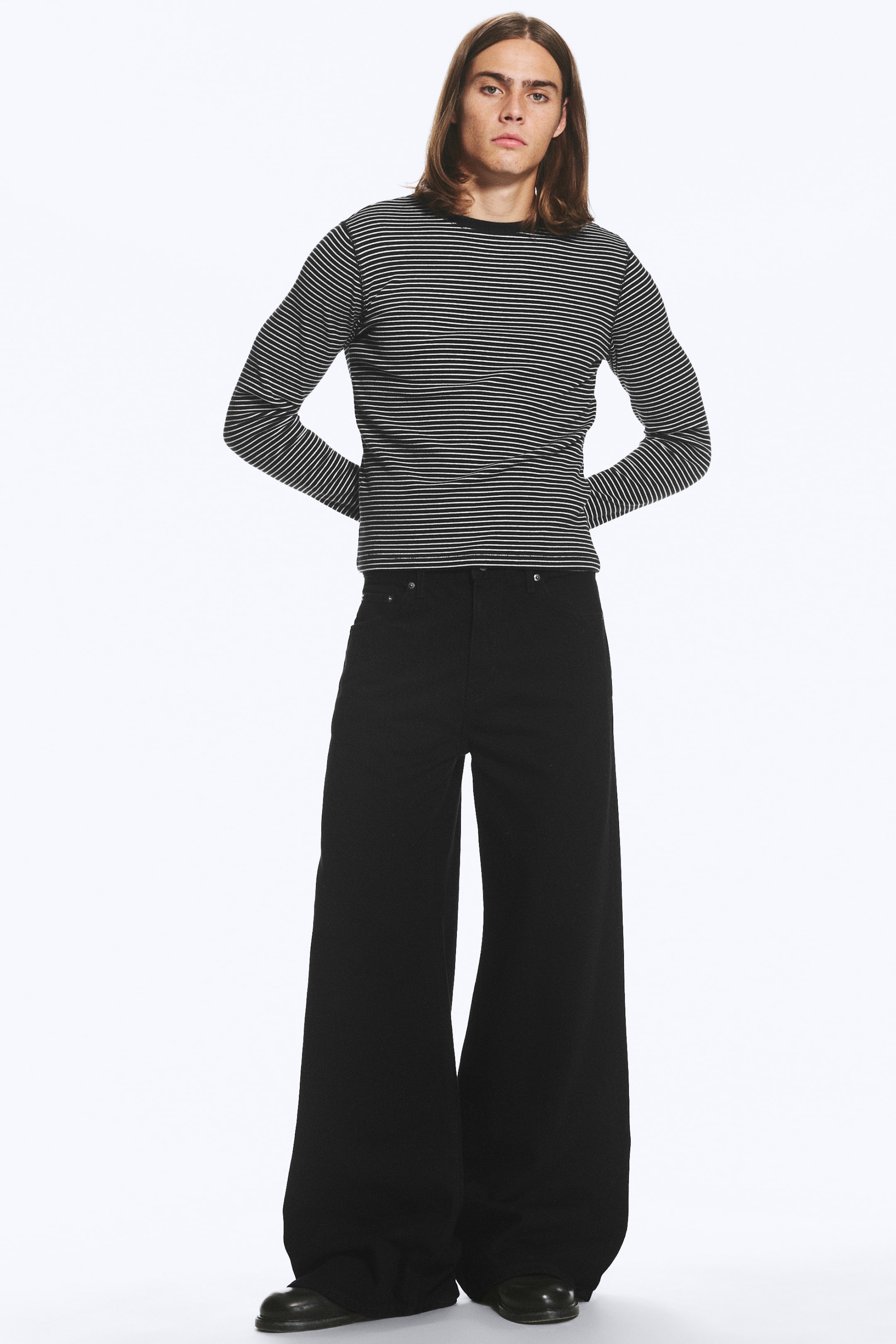 Grotere afbeelding bekijken: Zwarte loose fit jeans met wijde pijpen en een middelhoge taille worden gedragen door het model. De jeans hebben zichtbare zakken aan de voorkant en bedekken zwarte schoenen.