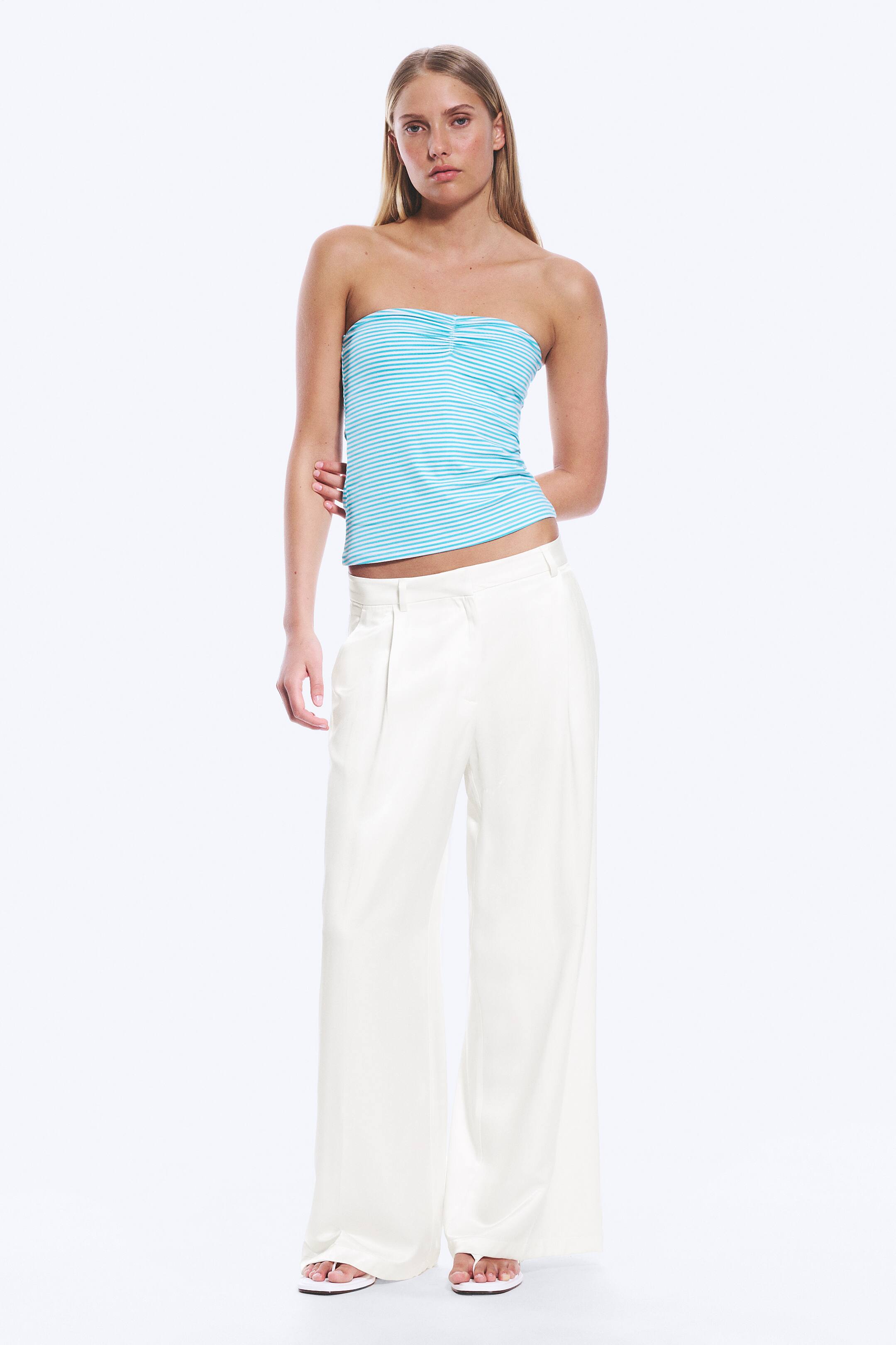 Преглед на по-голямо изображение: Светлосиньо и бяло райе бюстие без презрамки, което се отличава със събрана централна част на бюста, е представено. То е комбинирано с бели, високо талияни, широки панталони с предни плисета.