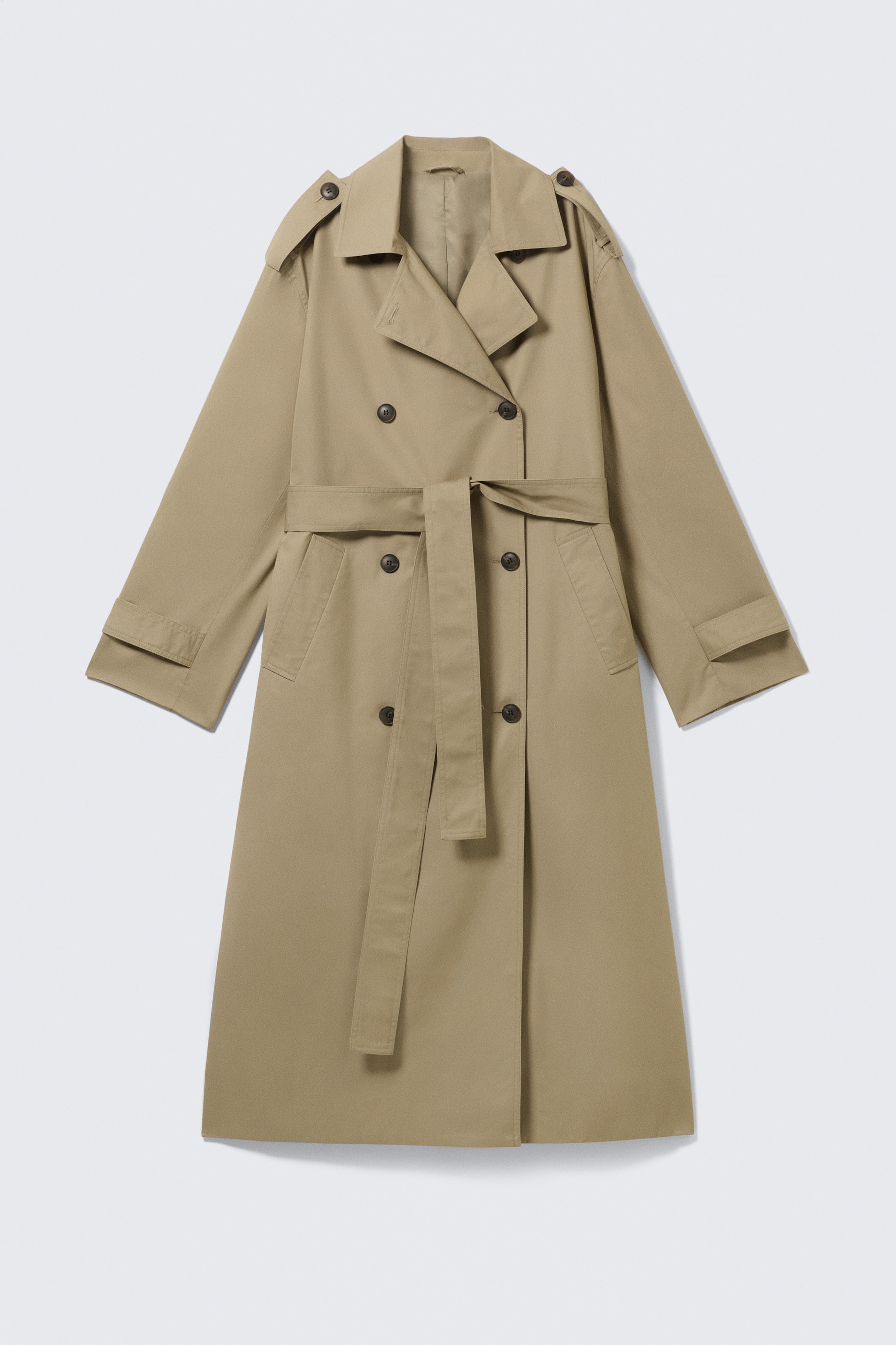 Größeres Bild ansehen: Ein übergroßer, hellbrauner, zweireihiger Trenchcoat ist von vorne zu sehen, mit Epauletten, einem Sturmklappe, einem passenden Stoffgürtel, der in der Taille gebunden ist, schrägen Leistentaschen und verstellbaren Riemen an den Ärmelabschlüssen.