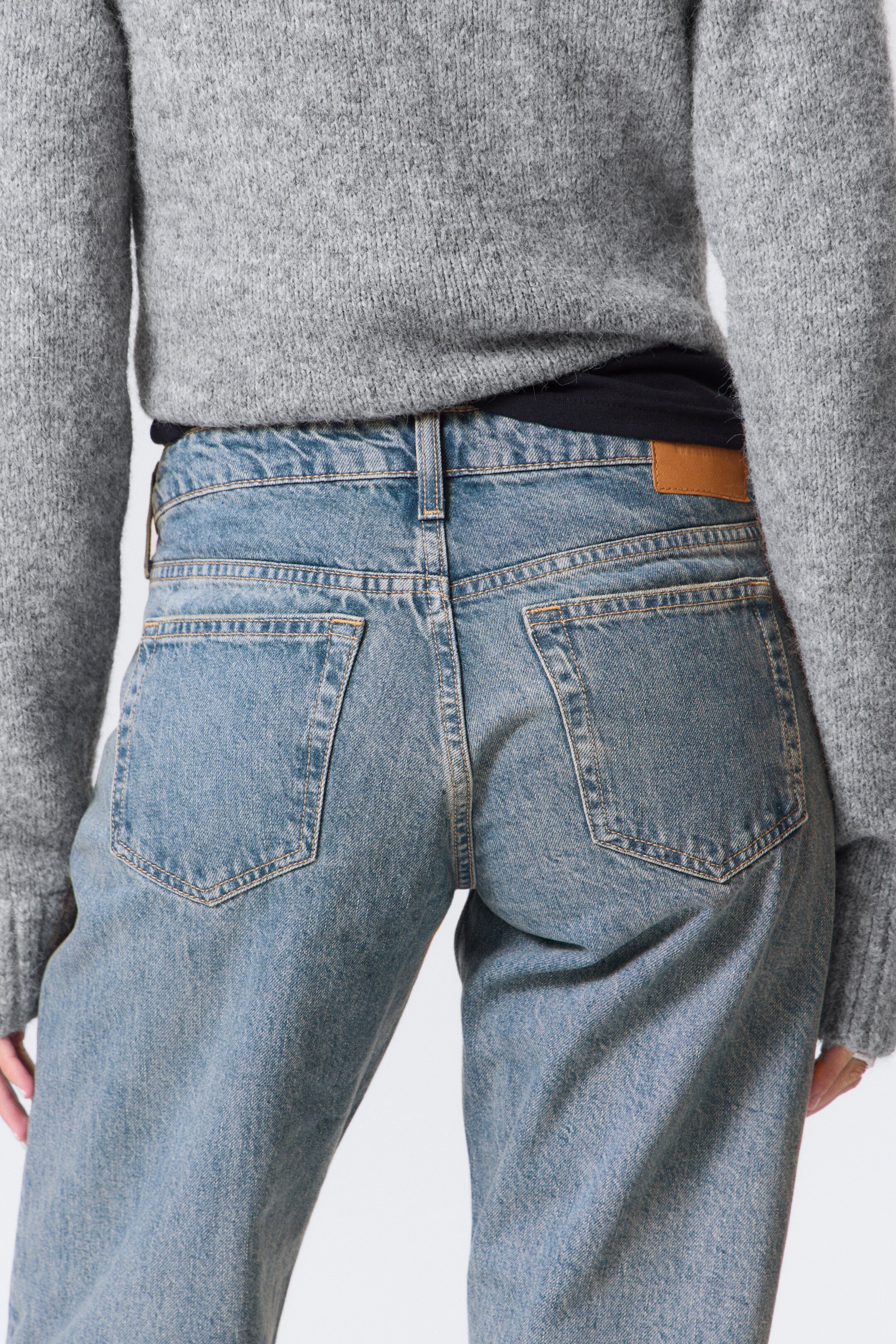 Agrandir l'image: Un jean en denim bleu clair est présenté de dos, avec des coutures contrastées, une taille haute avec des passants de ceinture et deux poches plaquées à l'arrière. Une étiquette marron est également visible sur le côté droit de la ceinture.
