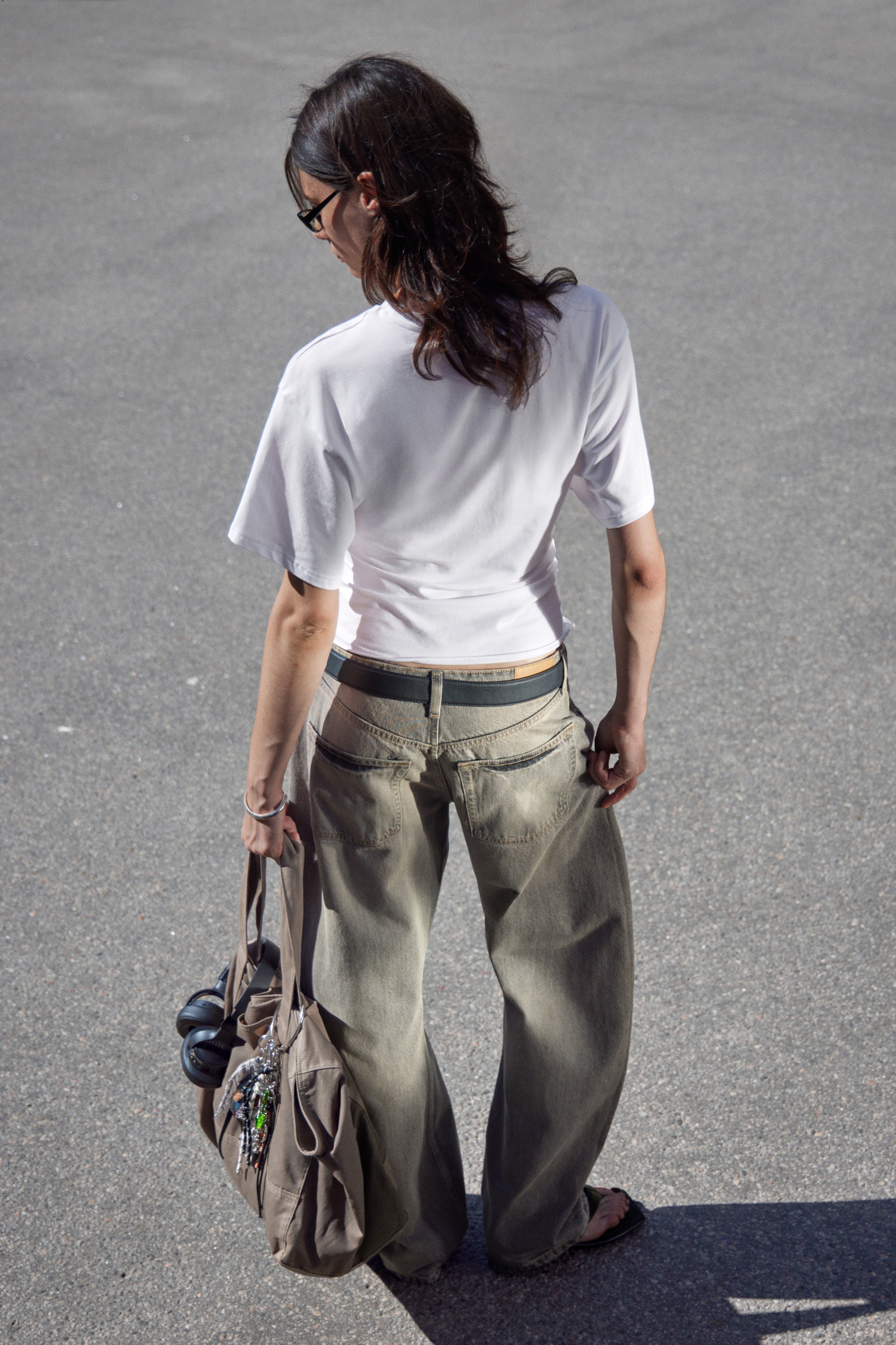 View larger image: A white, short-sleeved t-shirt with a relaxed fit is being worn with loose-fitting, wide-leg khaki jeans, cinched by a dark belt. The ensemble is viewed from the back, highlighting the casual drape of the garments.