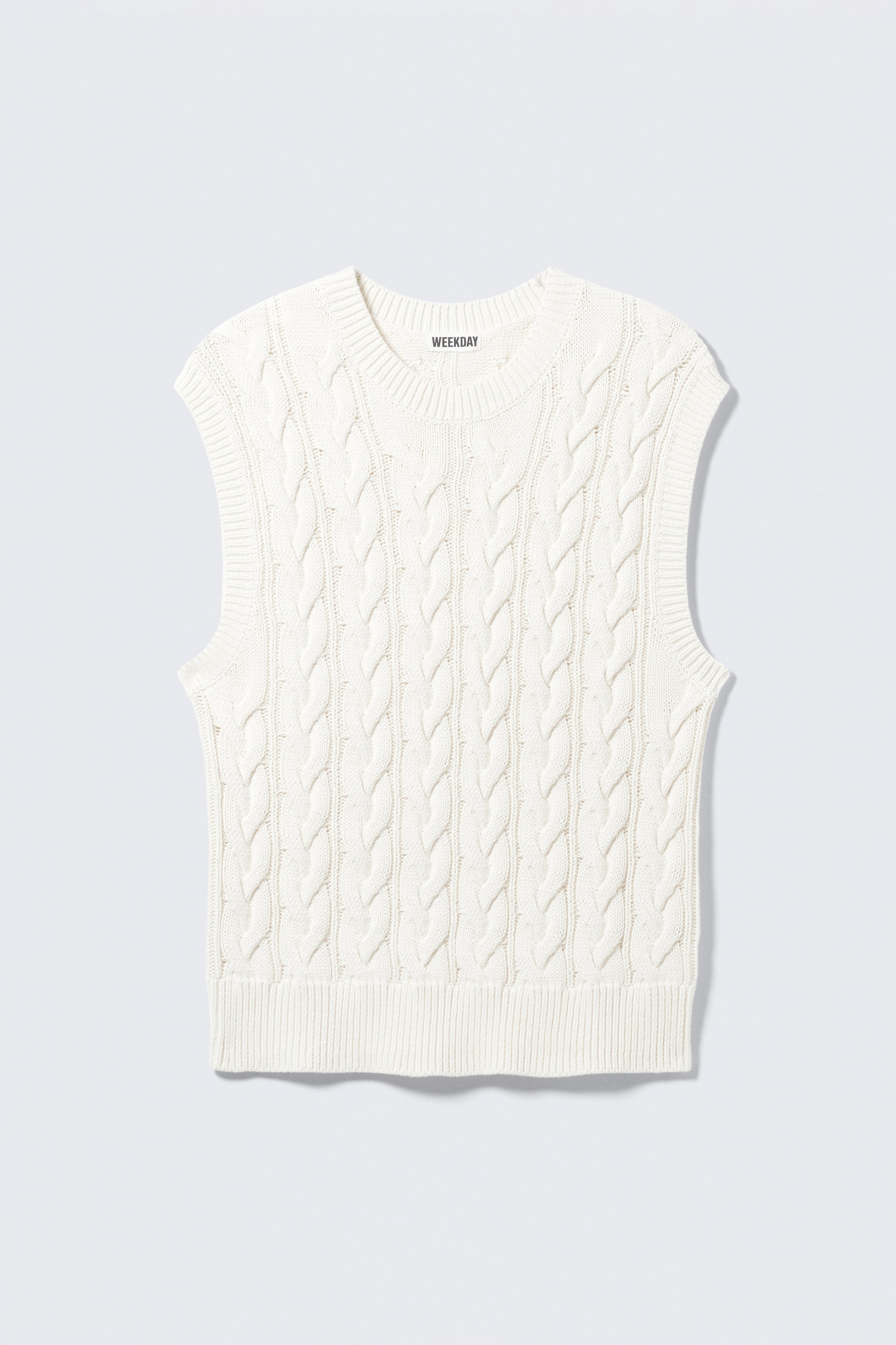 View larger image: A cream sleeveless sweater is featuring a cable knit pattern throughout its body, with a ribbed round neckline, ribbed armholes, and a ribbed hem.