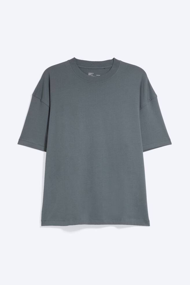 Een oversized boxy T-shirt in leigrijs wordt van voren getoond, met een geribde ronde hals, verlaagde schouders en wijde mouwen tot aan de elleboog. Het T-shirt heeft een losse, vierkante silhouet met een rechte zoom. - 1
