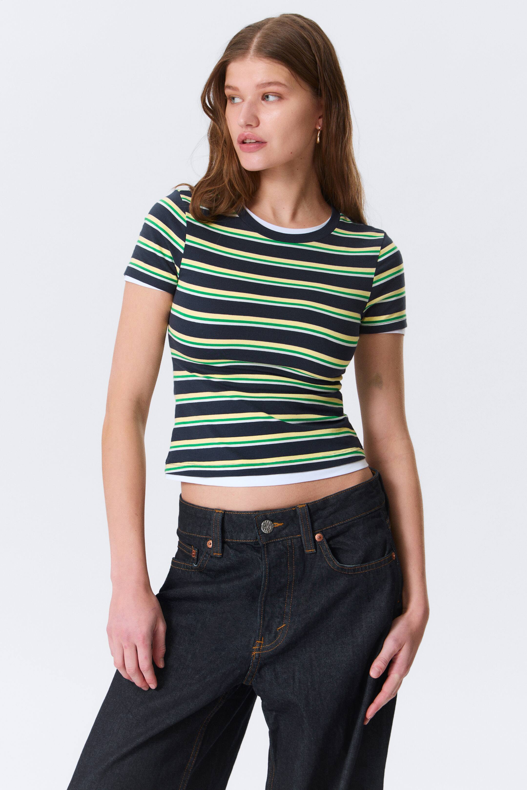 Vezi imaginea mai mare: Un tricou mulat, cu mâneci scurte, este prezentat din față. Prezintă dungi orizontale în nuanțe de bleumarin, galben, verde și alb, cu o bordură albă la gulerul rotund. Tivul scurt dezvăluie un strat alb dedesubt.