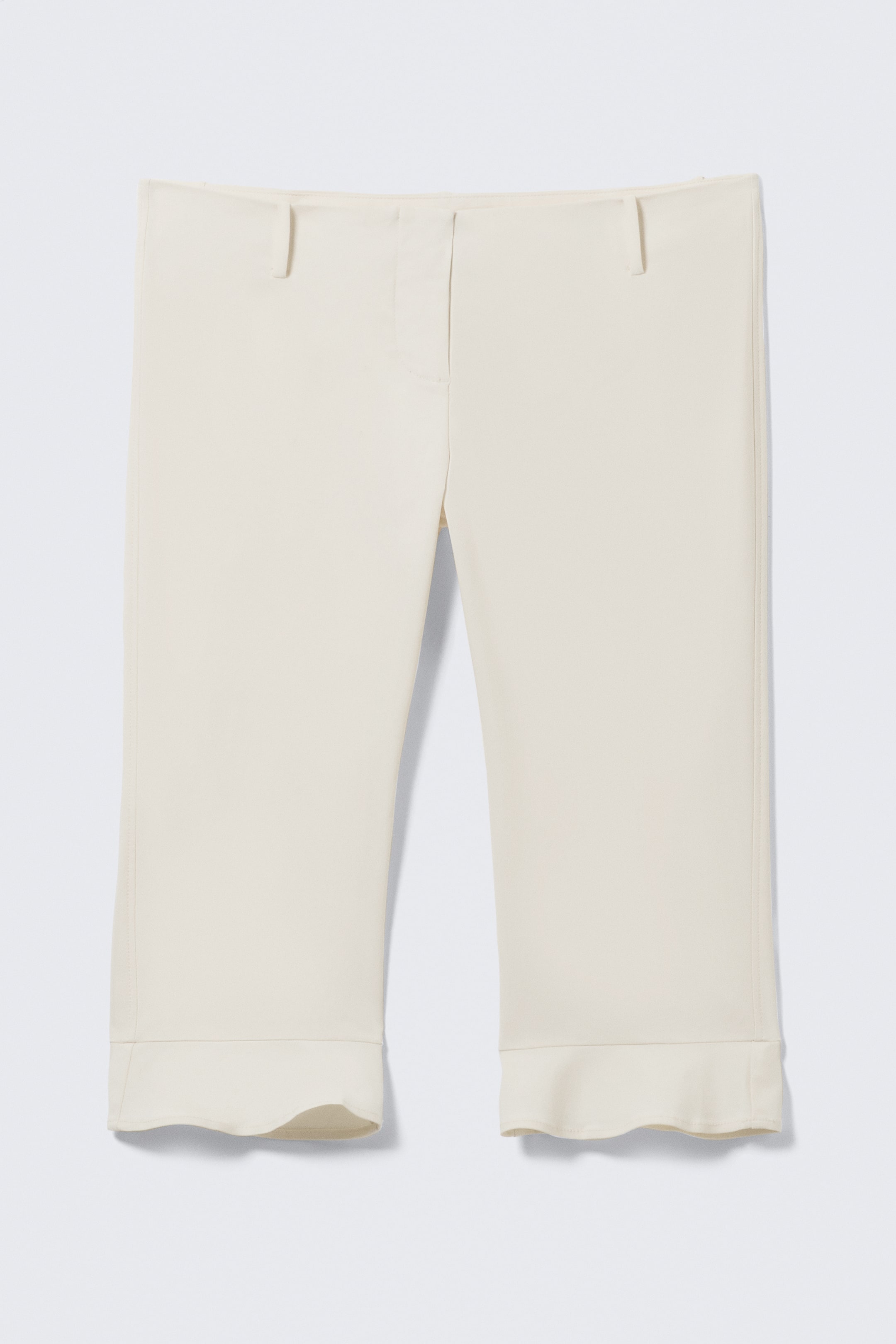 Visualizza immagine più grande: Pantaloni cropped color crema sono esposti frontalmente, mostrando una cintura piatta con tre passanti per cintura visibili. I pantaloni presentano gambe dritte e terminano con polsini ampi e leggermente smerlati.