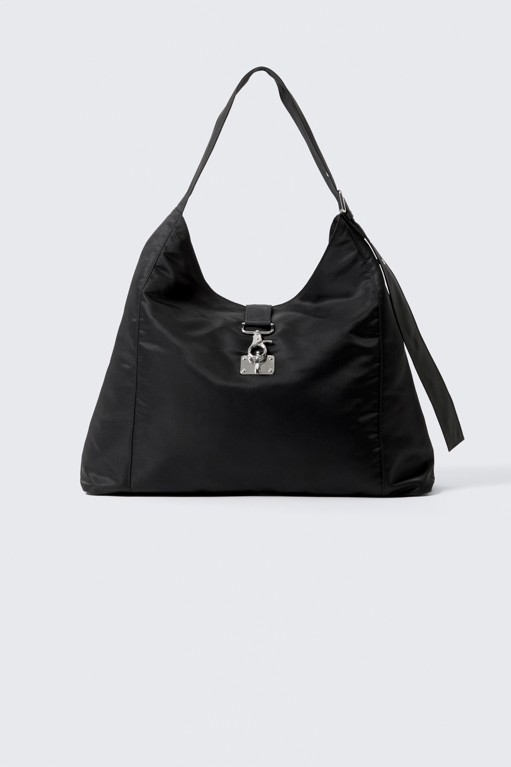 Größeres Bild ansehen: Eine schwarze Schultertasche, präsentiert von FRONT, zeichnet sich durch eine lässige, halbmondförmige Silhouette aus, die aus glattem Nylonstoff gefertigt ist. Sie ist mit einem einzelnen, breiten Schulterriemen und einem auffälligen silberfarbenen Metallschließelement an der Vorderseite ausgestattet, das eine rechteckige Platte und einen Drehverschluss umfasst.