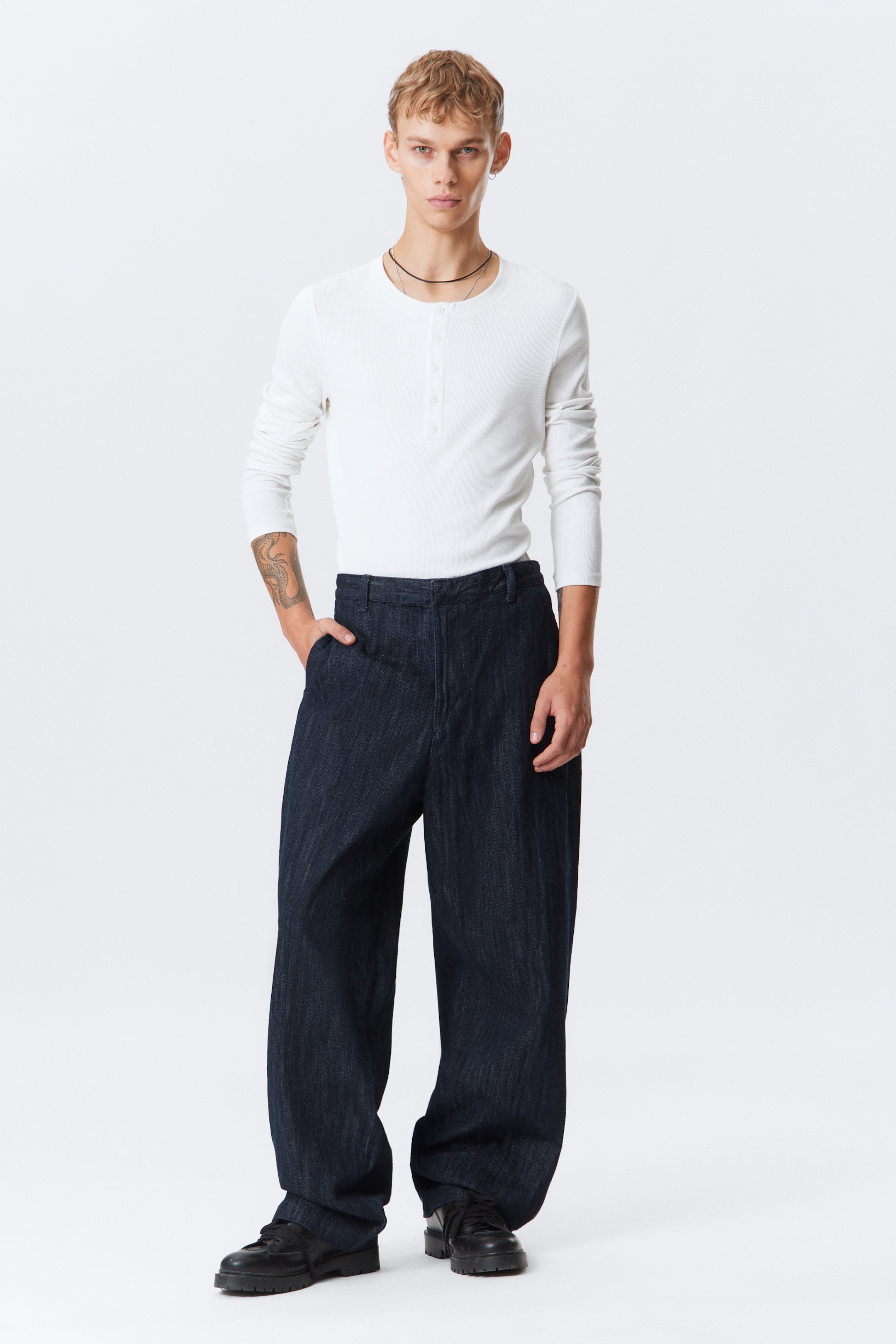 Ver imagen más grande: Pantalones azul oscuro de pierna ancha presentan un sutil tejido texturizado vertical, con un corte de cintura alta y ajuste suelto que se acumula ligeramente sobre los zapatos, mostrados desde un ángulo frontal completo.