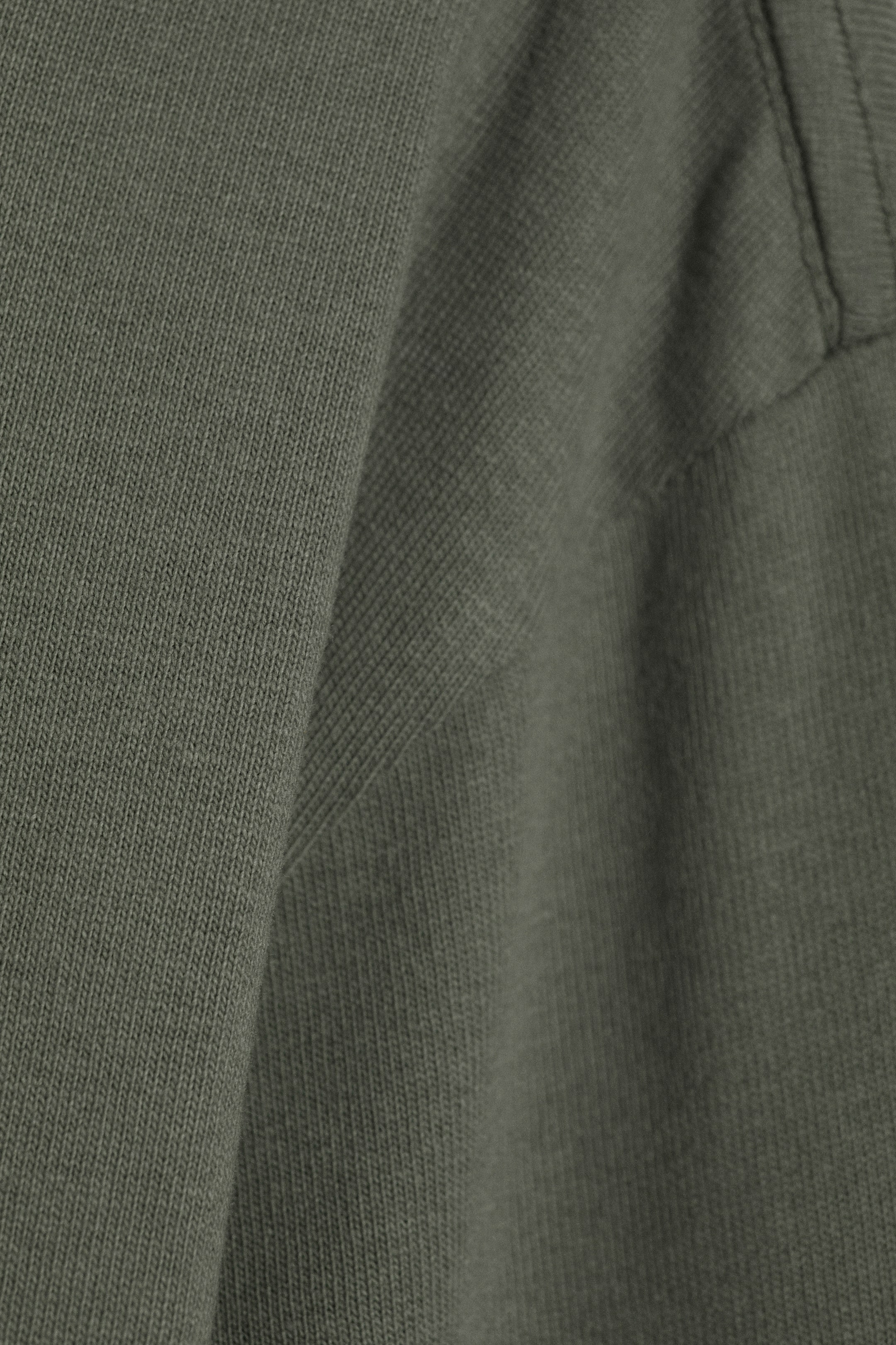 Ver imagen más grande: Una camiseta de manga larga muestra su tejido de punto de algodón en color verde oliva, con un detalle de punto acanalado visible a la izquierda, unido por una costura.