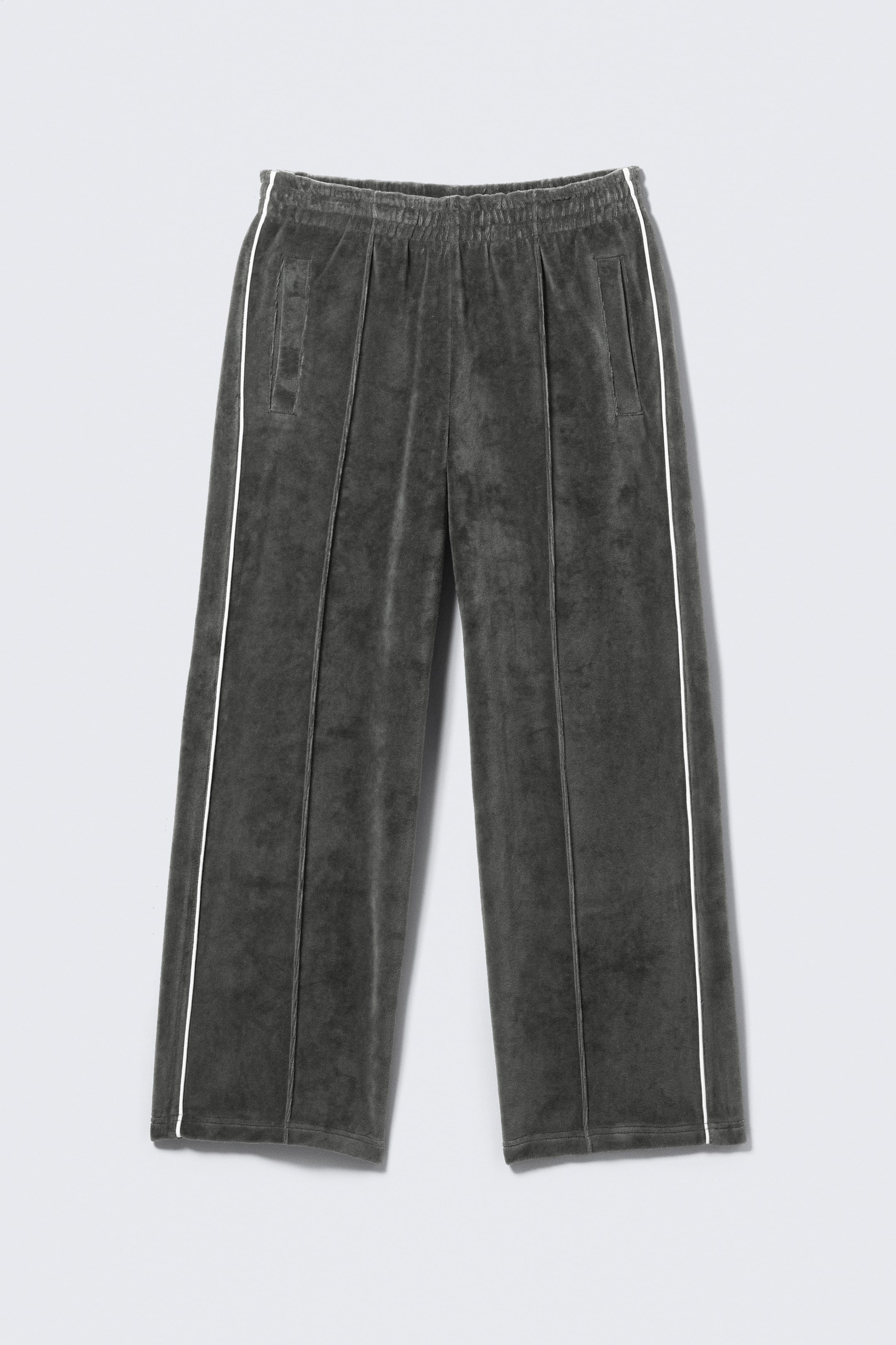 View larger image: A pair of dark grey velour trousers is presented in a front view, featuring an elasticated waistband and side seam pockets. White stripes run down each side seam, and vertical stitched creases detail the front of each wide leg.