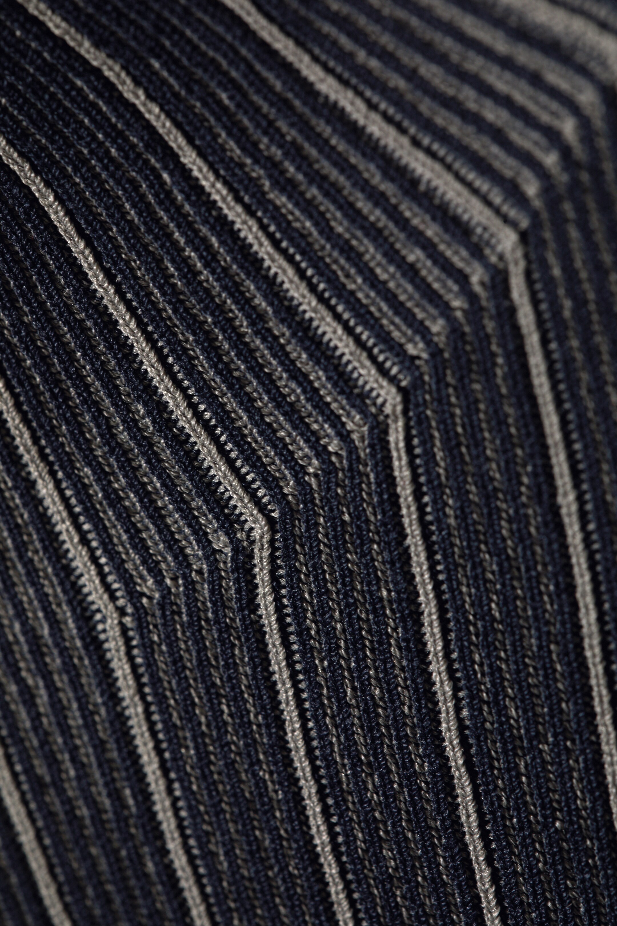 Größeres Bild ansehen: Ein Slim-Fit-Rollkragenpullover wird in einer Nahaufnahme präsentiert, die seine feine Rippstrickstruktur hervorhebt. Der Stoff zeigt abwechselnd dunkle und helle vertikale Rippen, die markante, winklige Muster bilden.