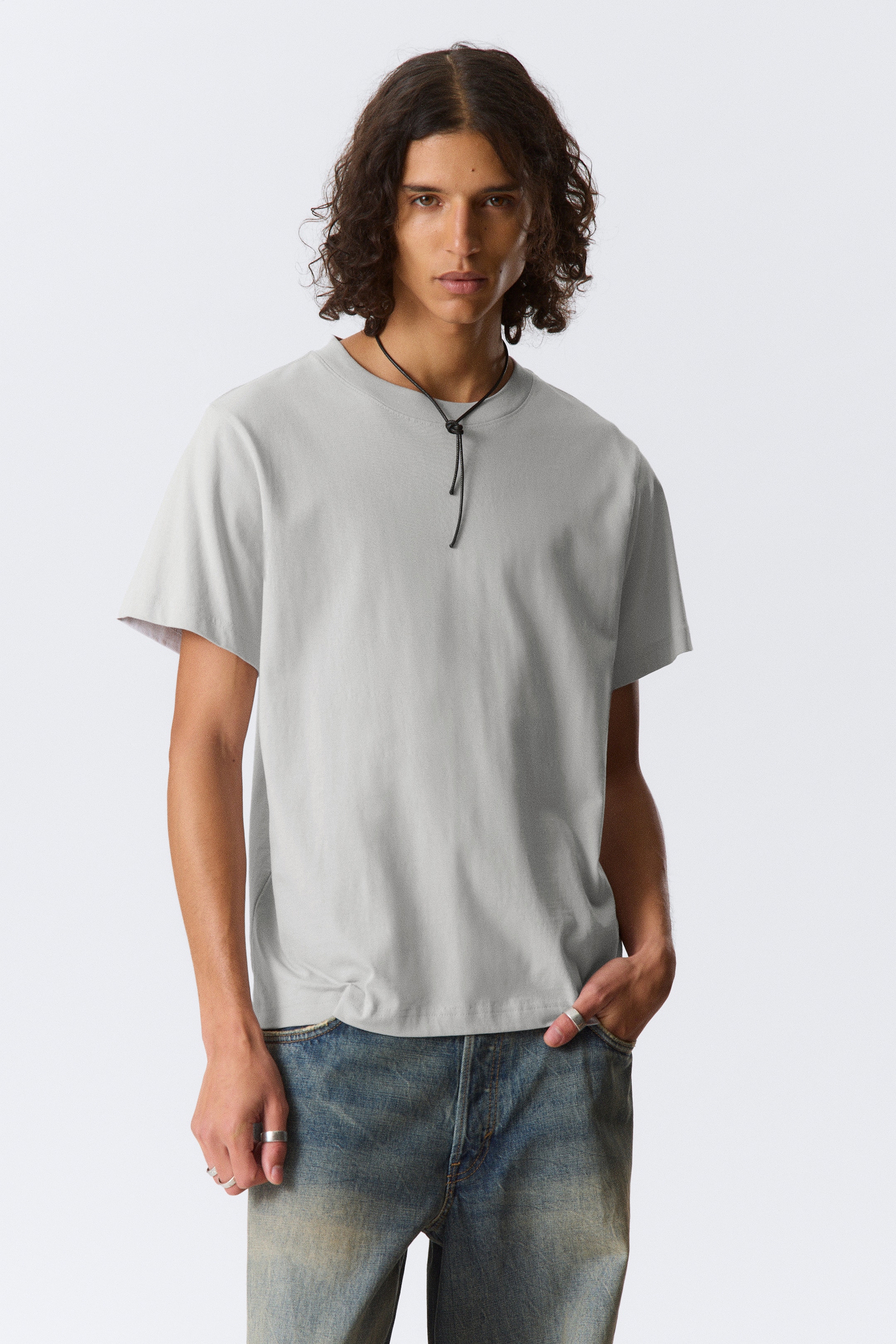 Visualizza immagine più grande: Una t-shirt grigio chiaro è presentata, rivolta in avanti. Presenta un girocollo e maniche corte, con il tessuto che cade morbidamente per una vestibilità rilassata.