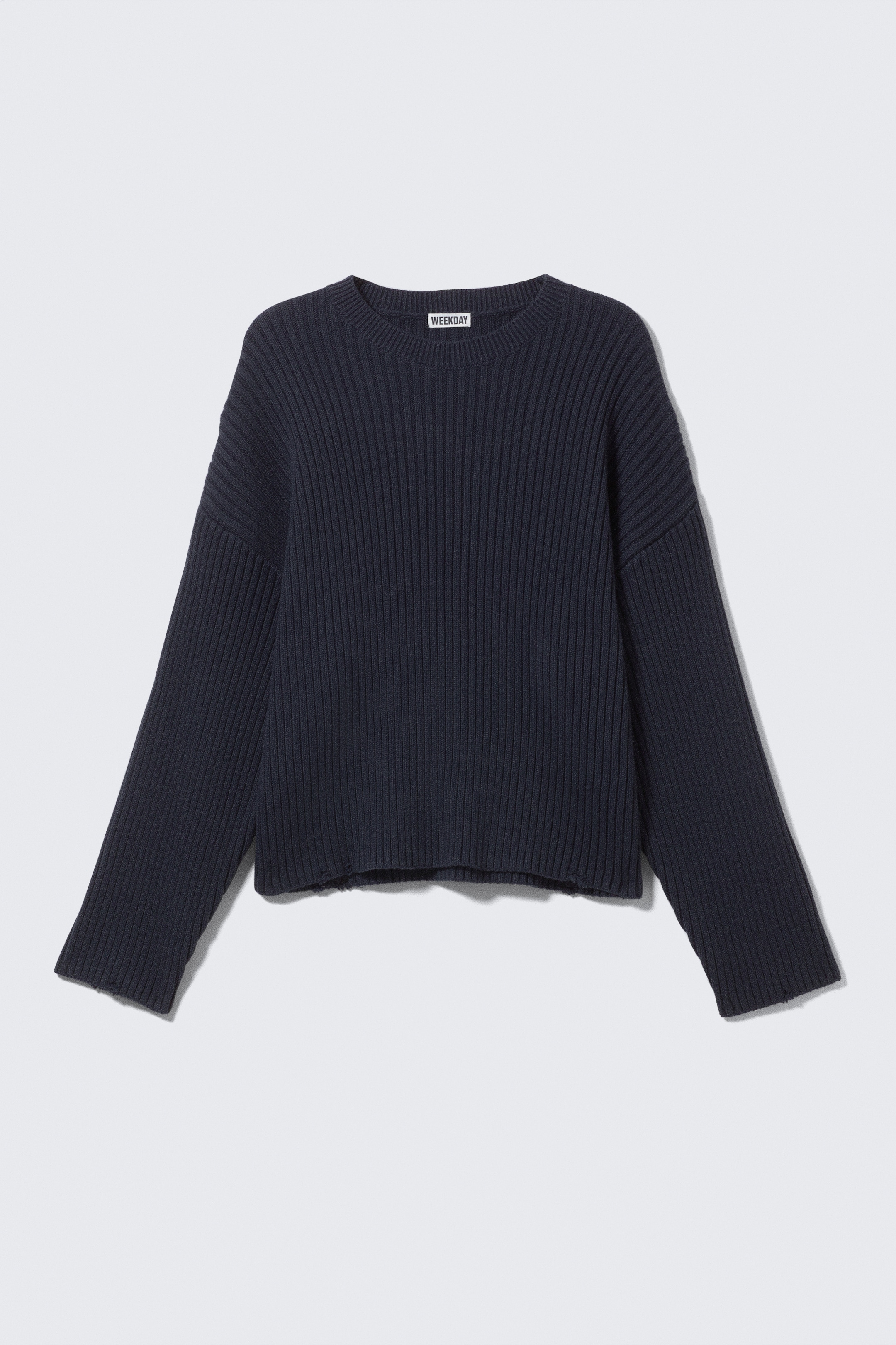 Visualizza immagine più grande: Un maglione in cotone a coste di colore blu scuro è mostrato dalla parte anteriore, caratterizzato da una vestibilità ampia con spalle scese. È progettato con un classico scollo a girocollo e orli sfrangiati sul fondo e sui polsini.